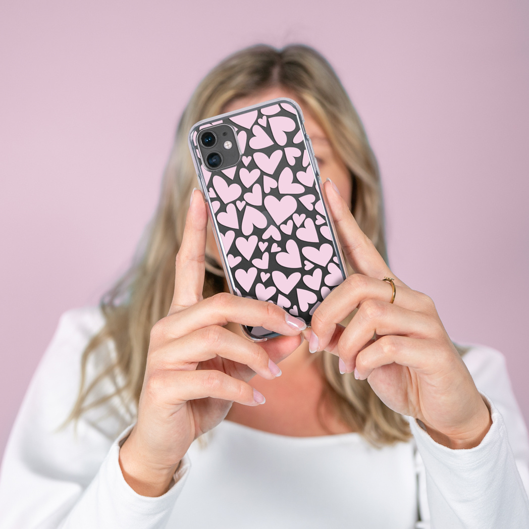 Une femme tenant une coque de téléphone avec un motif de cœurs roses, montrant le motif et la caméra.
