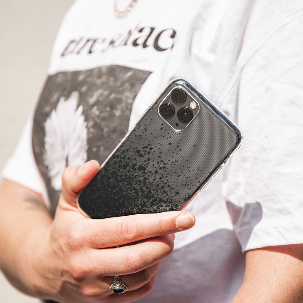 Person hält Telefon mit schwarzer und grauer Hülle. Weißes Hemd und Ring sichtbar.