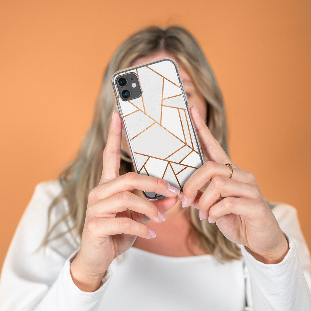 Femme tenant un téléphone montrant un design géométrique blanc et or.
