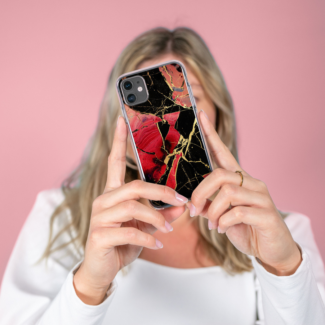 Vrouw houdt telefoon vast met zwart, rood en goud marmerontwerp op roze achtergrond.