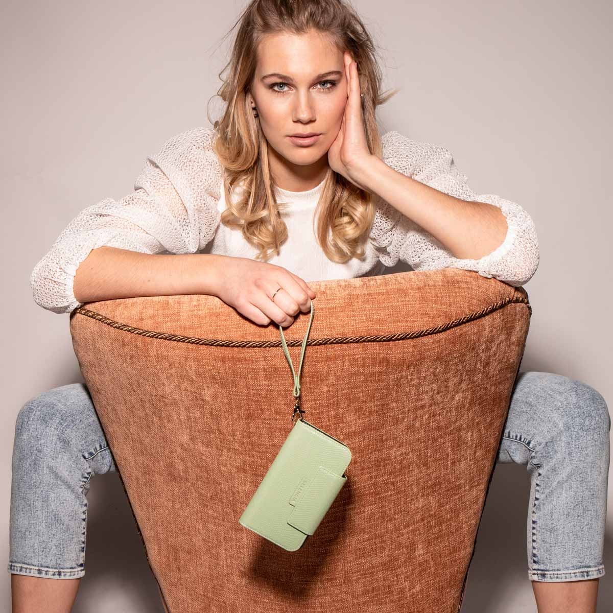 Een vrouw zit in een stoel en houdt een mintgroene telefoonportemonnee vast.