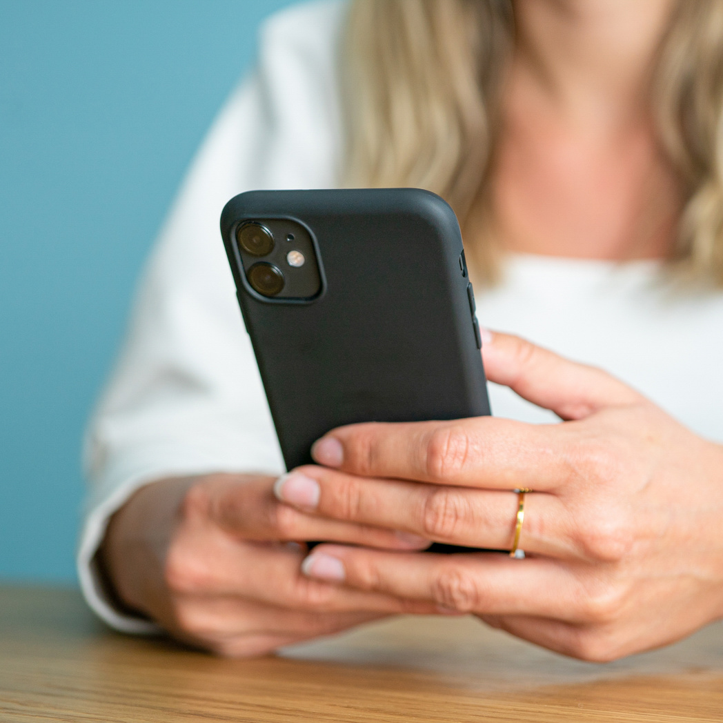 Eine Frau hält ein schwarzes Telefon vor blauem Hintergrund. An der rechten Hand trägt sie einen goldenen Ring.