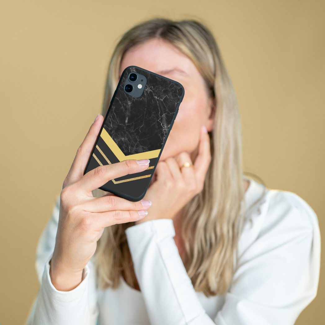 Vrouw houdt een zwarte telefoonhoes met een gouden ontwerp vast. De achtergrond is beige.