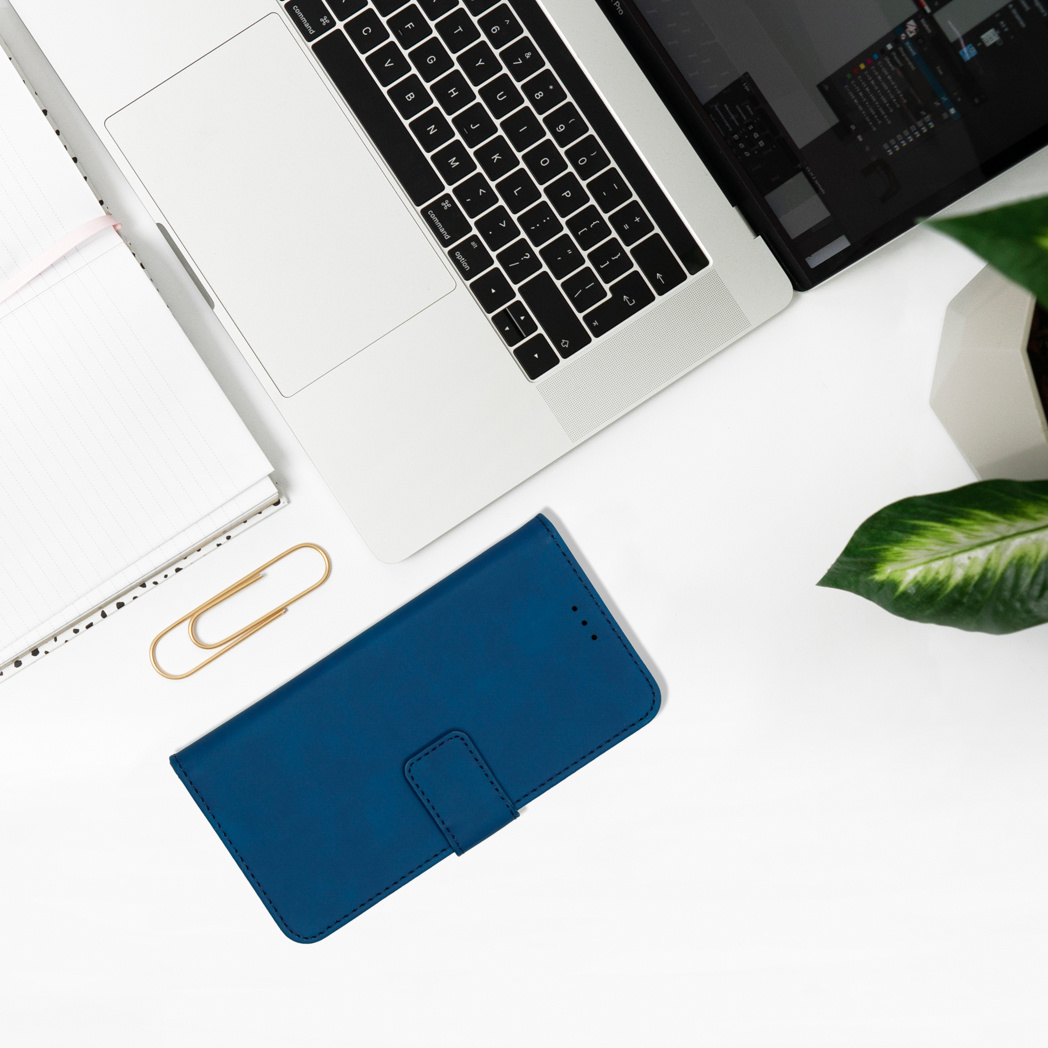 Un ordinateur portable, une coque de téléphone bleue, un trombone et un bloc-notes sont sur une table blanche.