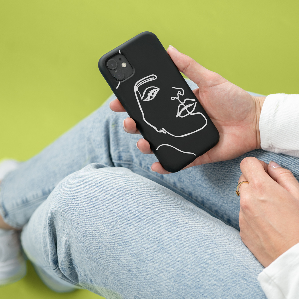 Persona che tiene un telefono con una custodia nera con un design di volto bianco. Sfondo di jeans.