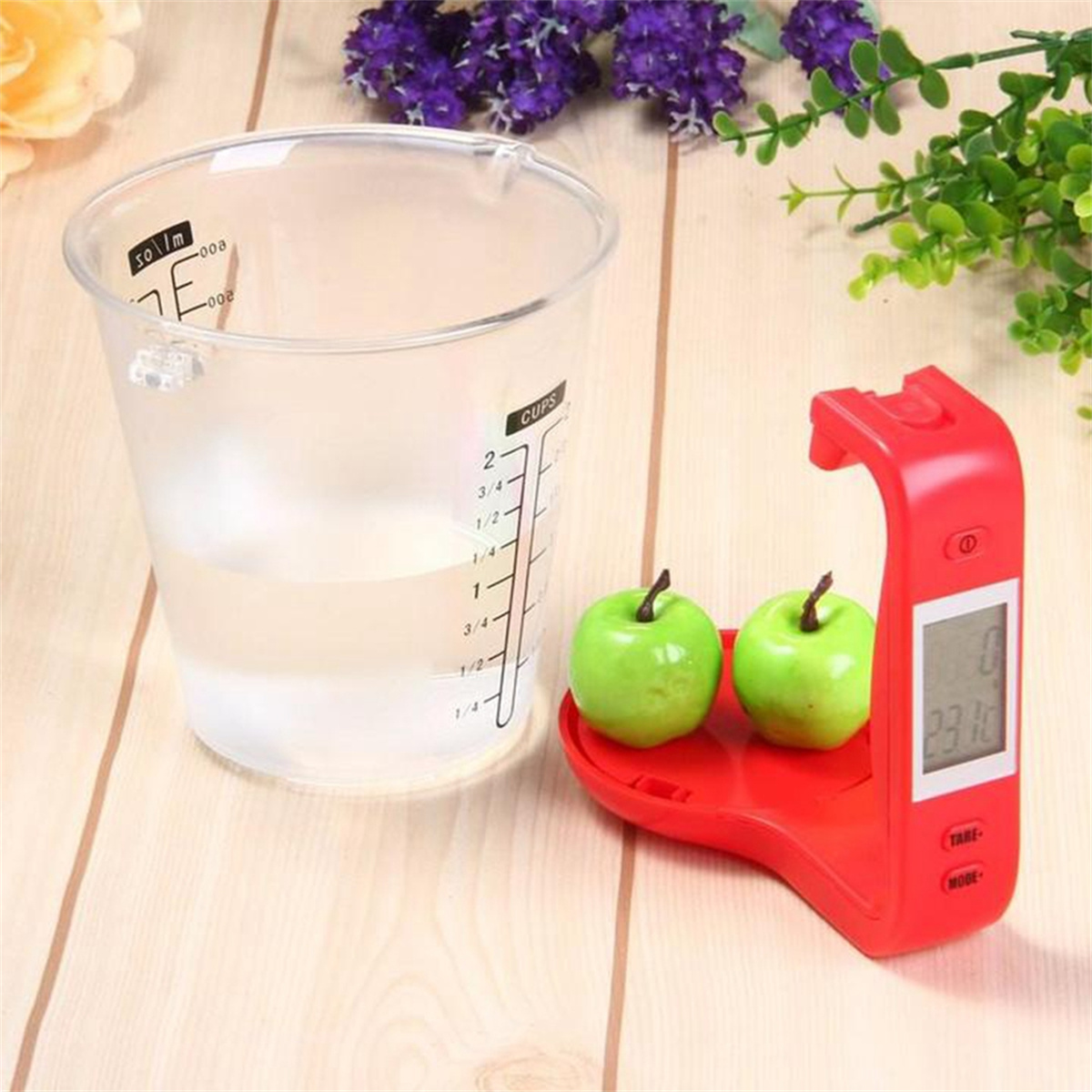 Ein Messbecher mit Wasser und eine rote Digitalwaage mit zwei grünen Äpfeln.