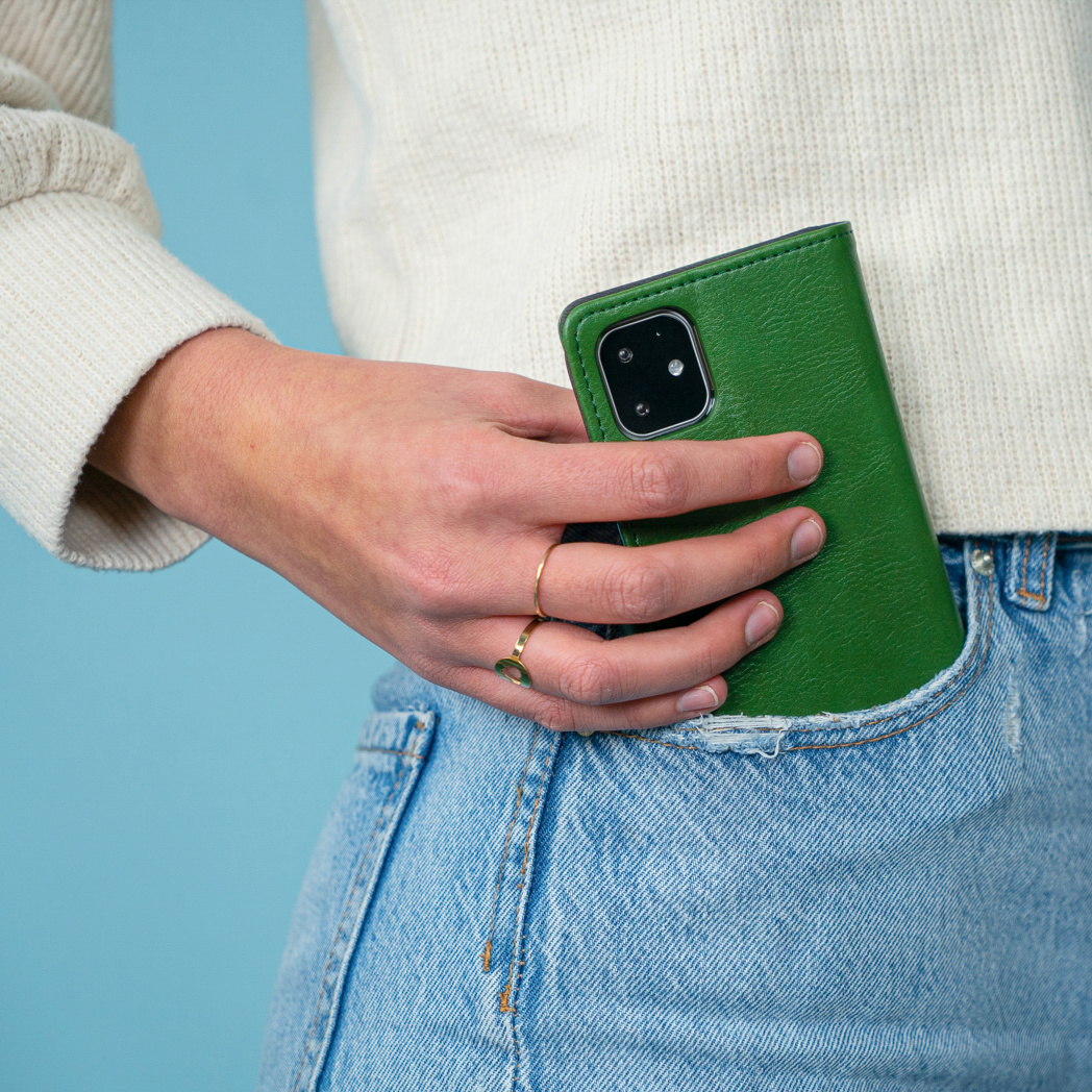 La main d'une personne tenant une coque de téléphone verte dans une poche de jean bleu.