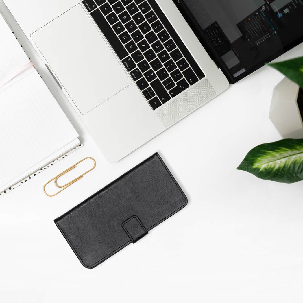 Laptop, notebook, and phone case on a white desk. There is a gold paperclip.