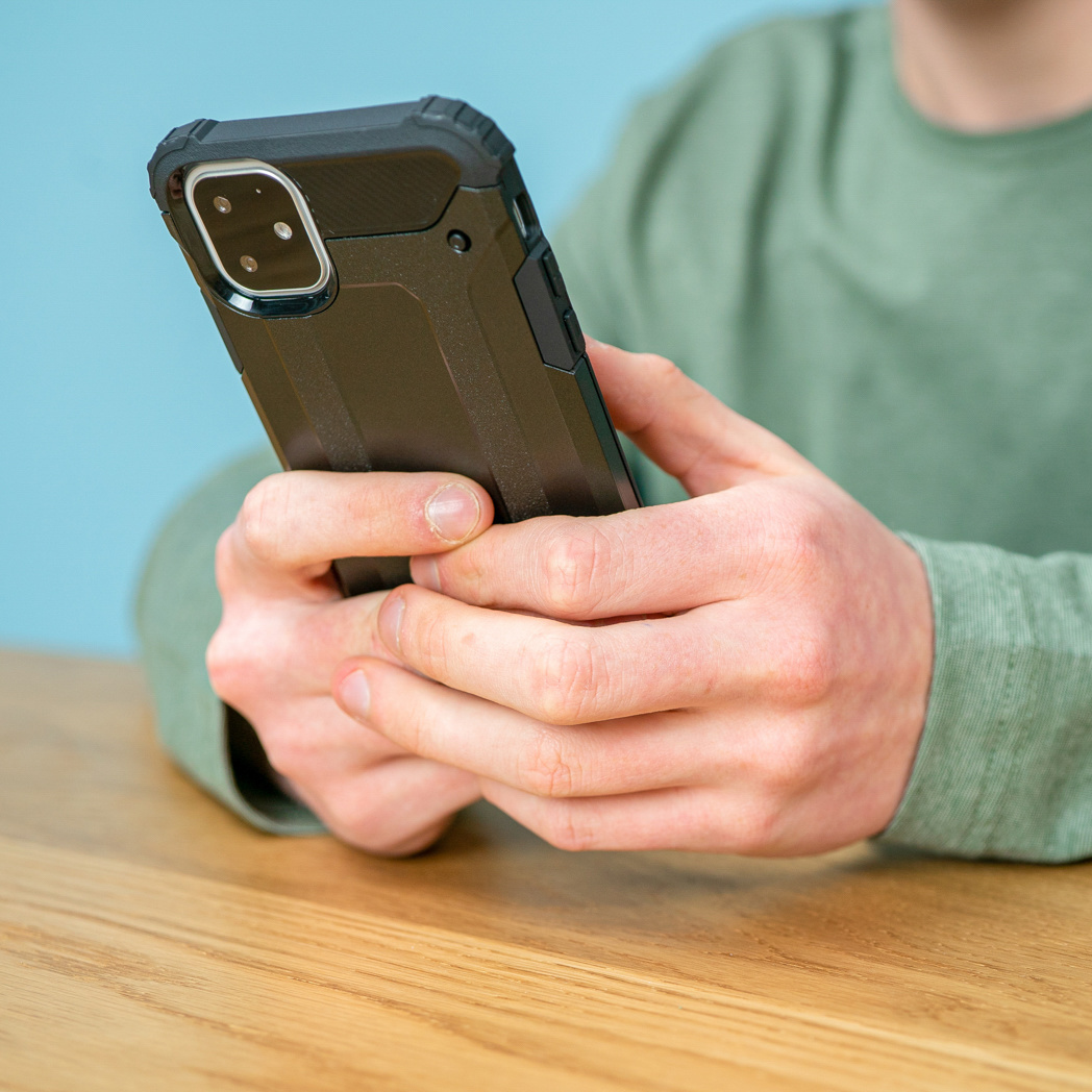 Persoon die een zwart telefoonhoesje vasthoudt, boven een houten tafel.