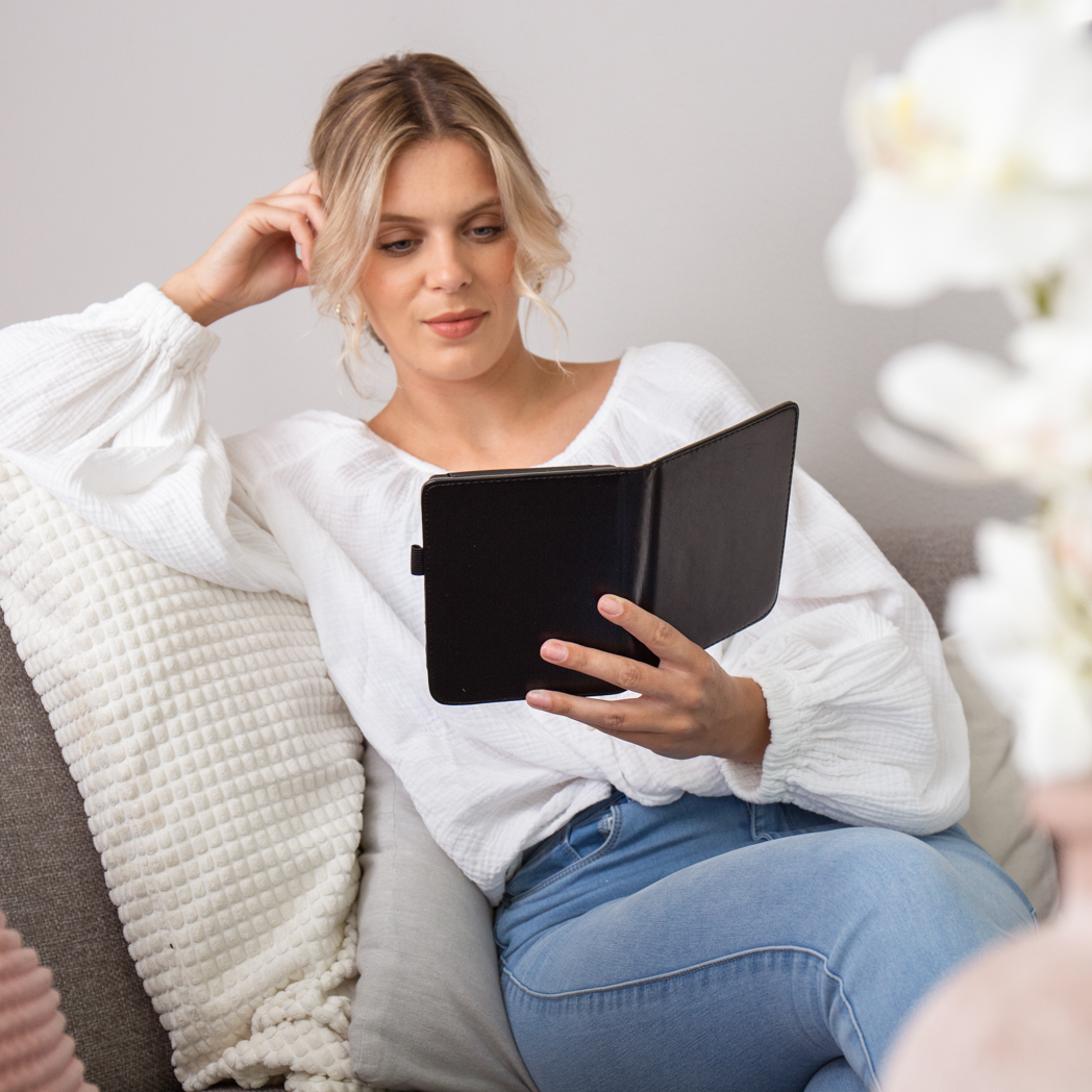 Blonde vrouw leest zwart boek, op grijze bank, bloemen op de voorgrond.