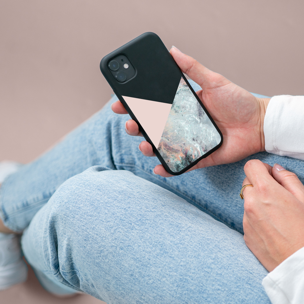 Persoon die een zwarte telefoon met een geometrisch ontwerp vasthoudt. Blauwe jeans en wit shirt.
