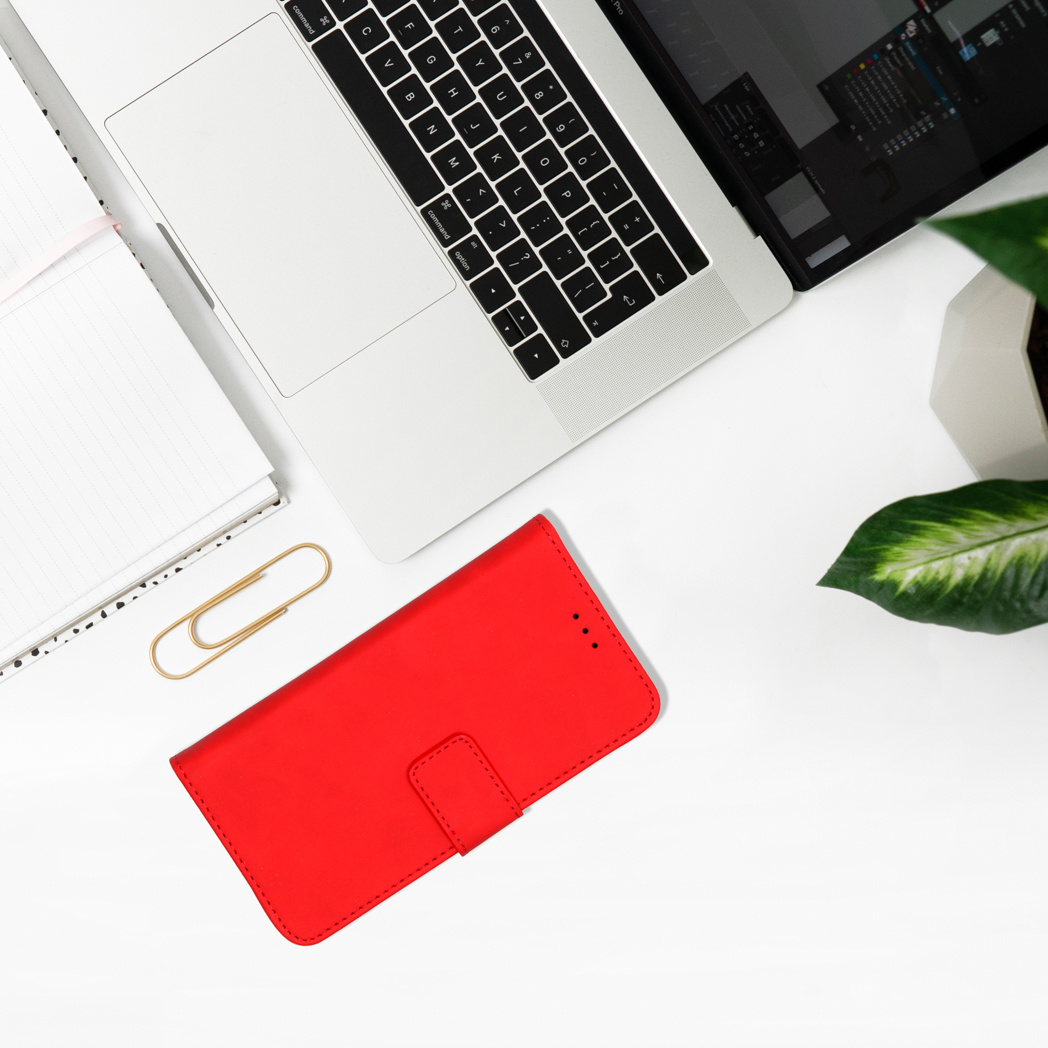 Une coque de téléphone rouge et un trombone sont sur un bureau blanc à côté d'un ordinateur portable et d'une plante.
