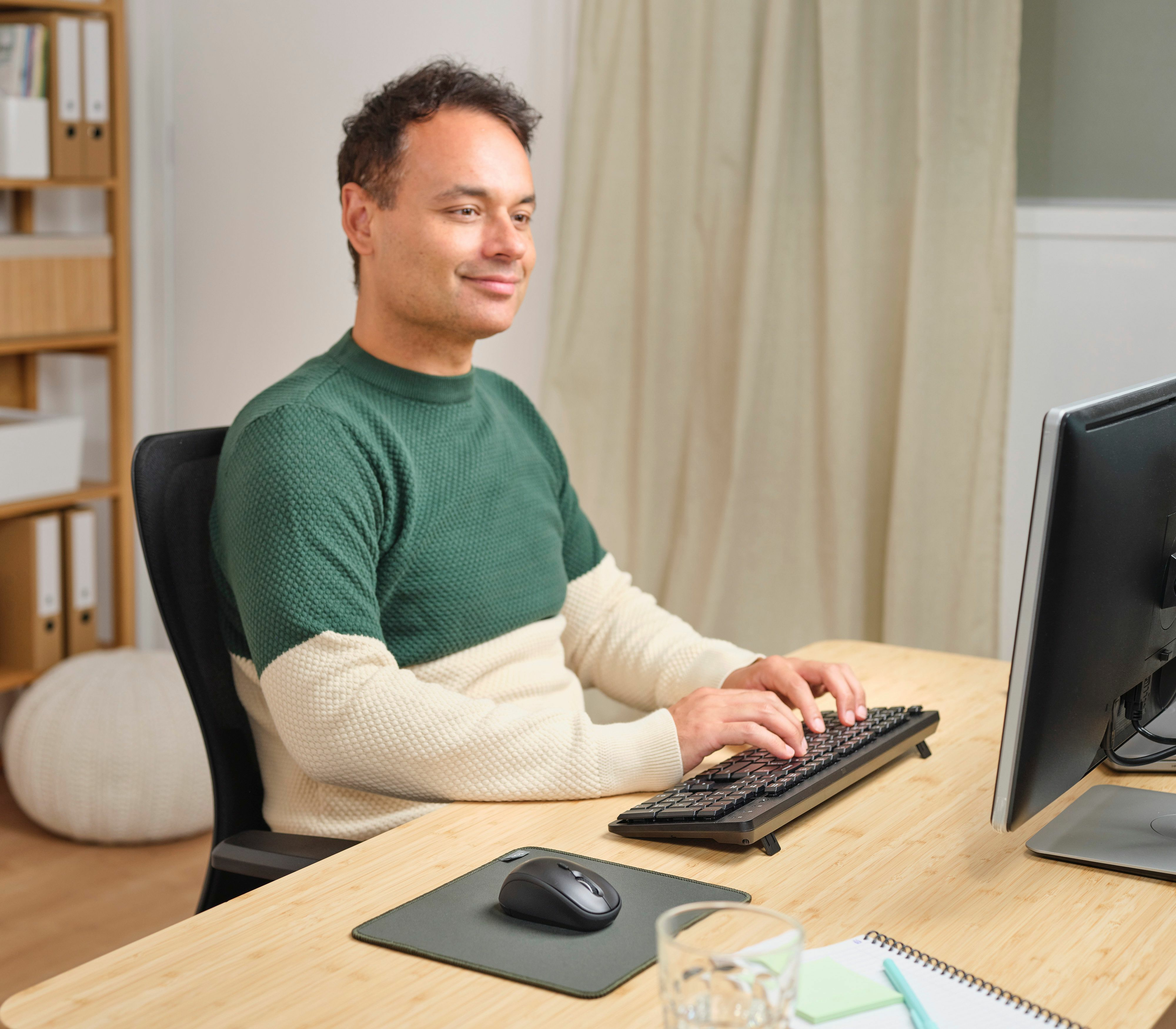 Mężczyzna piszący na klawiaturze, mysz na biurku, monitor, otoczenie biurowe.