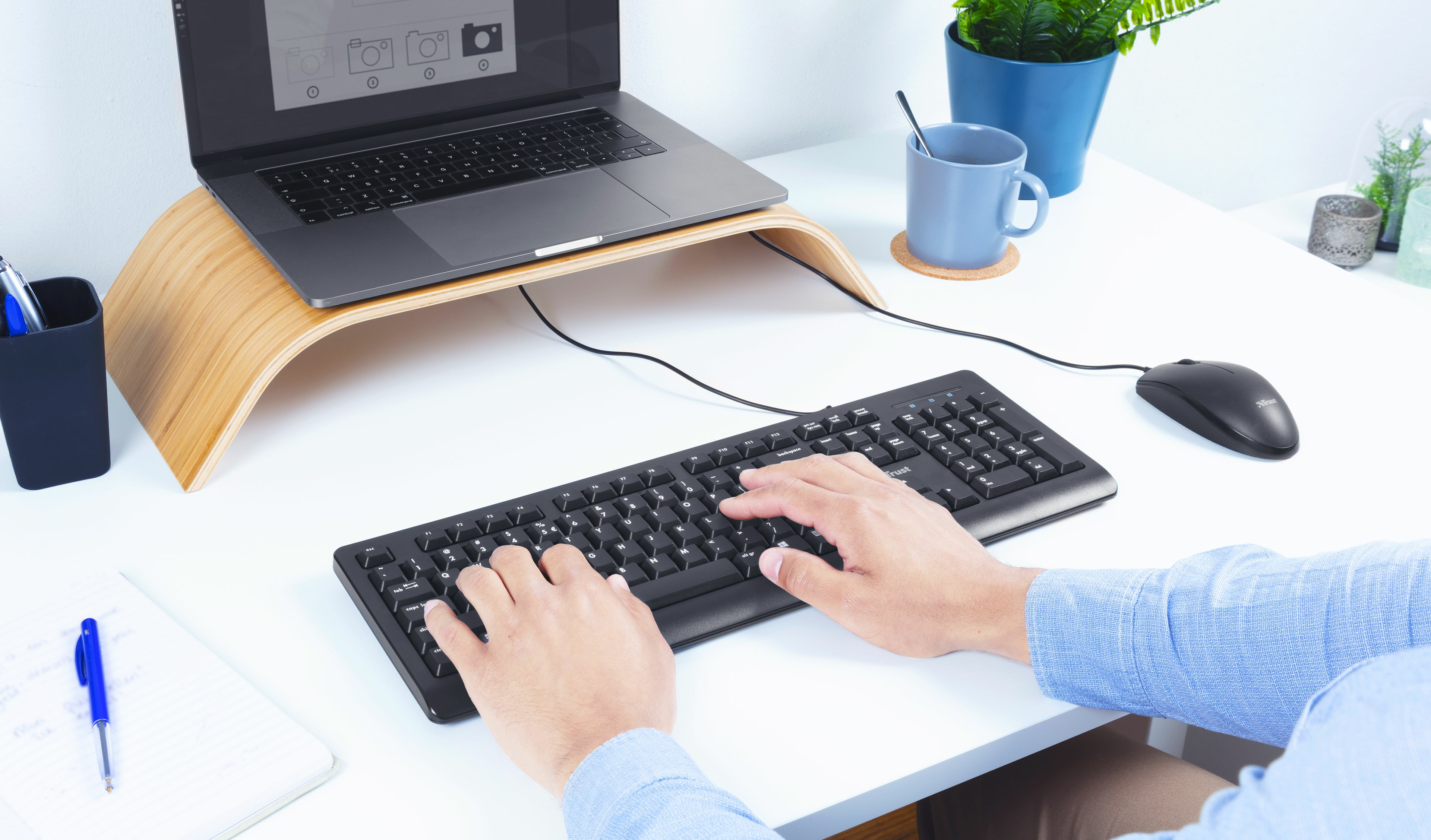 Biurko z laptopem, klawiaturą, myszką i osobą piszącą na klawiaturze.