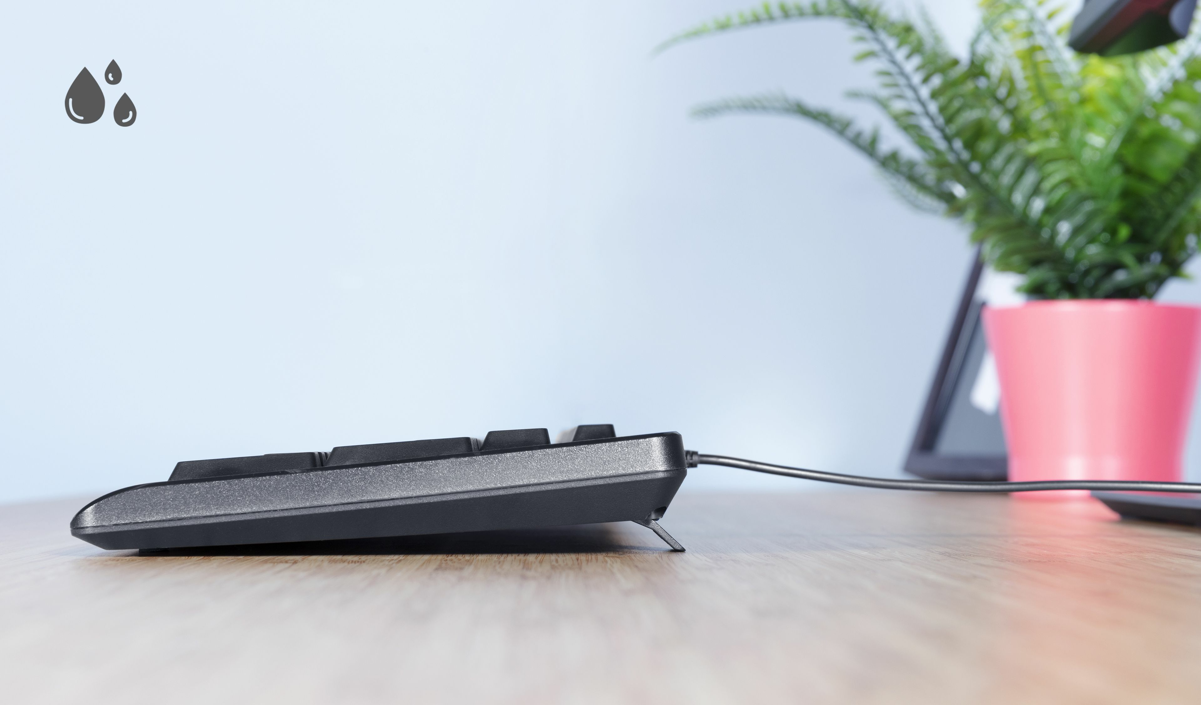 Widok z boku czarnej klawiatury na drewnianym stole. Obok klawiatury znajdują się krople wody.