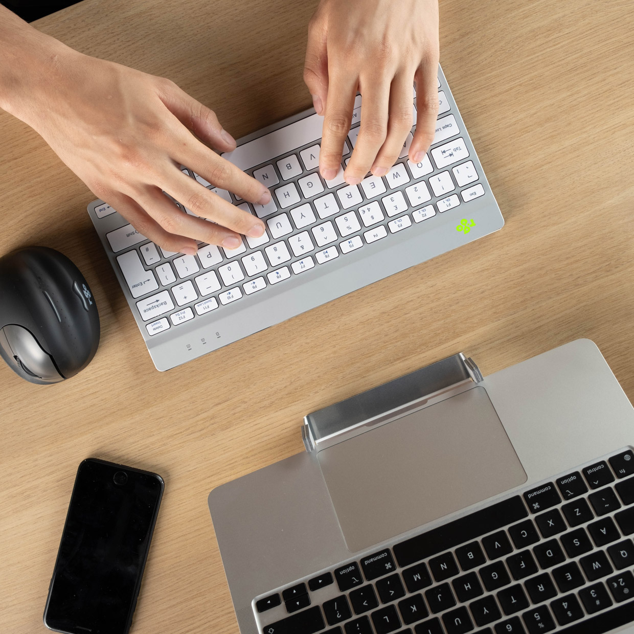 Mani su un tavolo che digitano su una piccola tastiera argentata, con un mouse e un laptop.