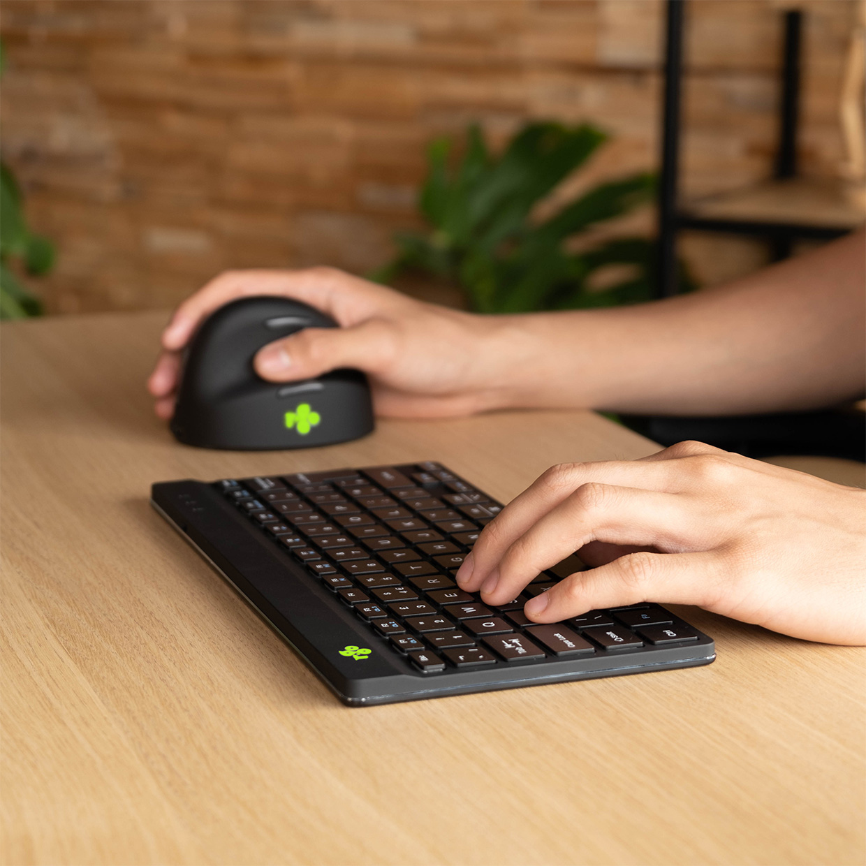 Hands typing on a keyboard and a mouse on a wooden table.