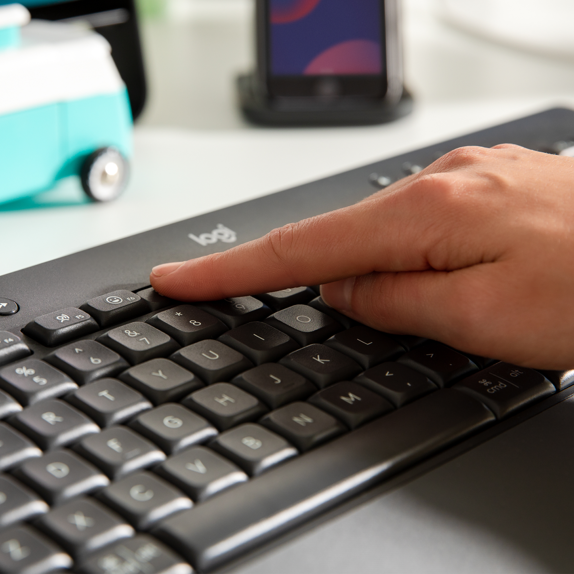 Dłoń naciskająca przycisk na czarnej klawiaturze Logitech.