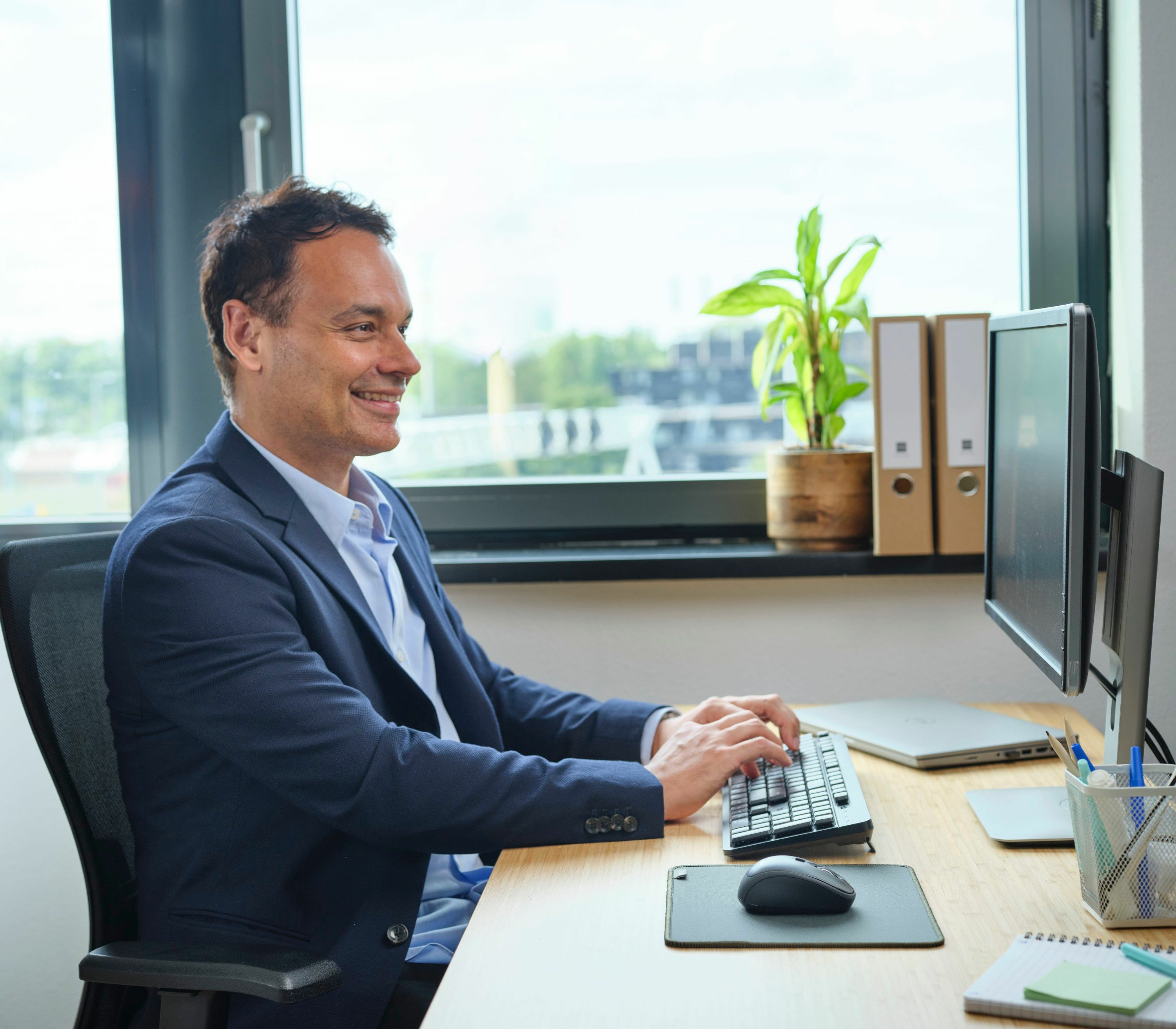 Mężczyzna używający klawiatury i myszy. Ma na sobie niebieski garnitur i patrzy na komputer.