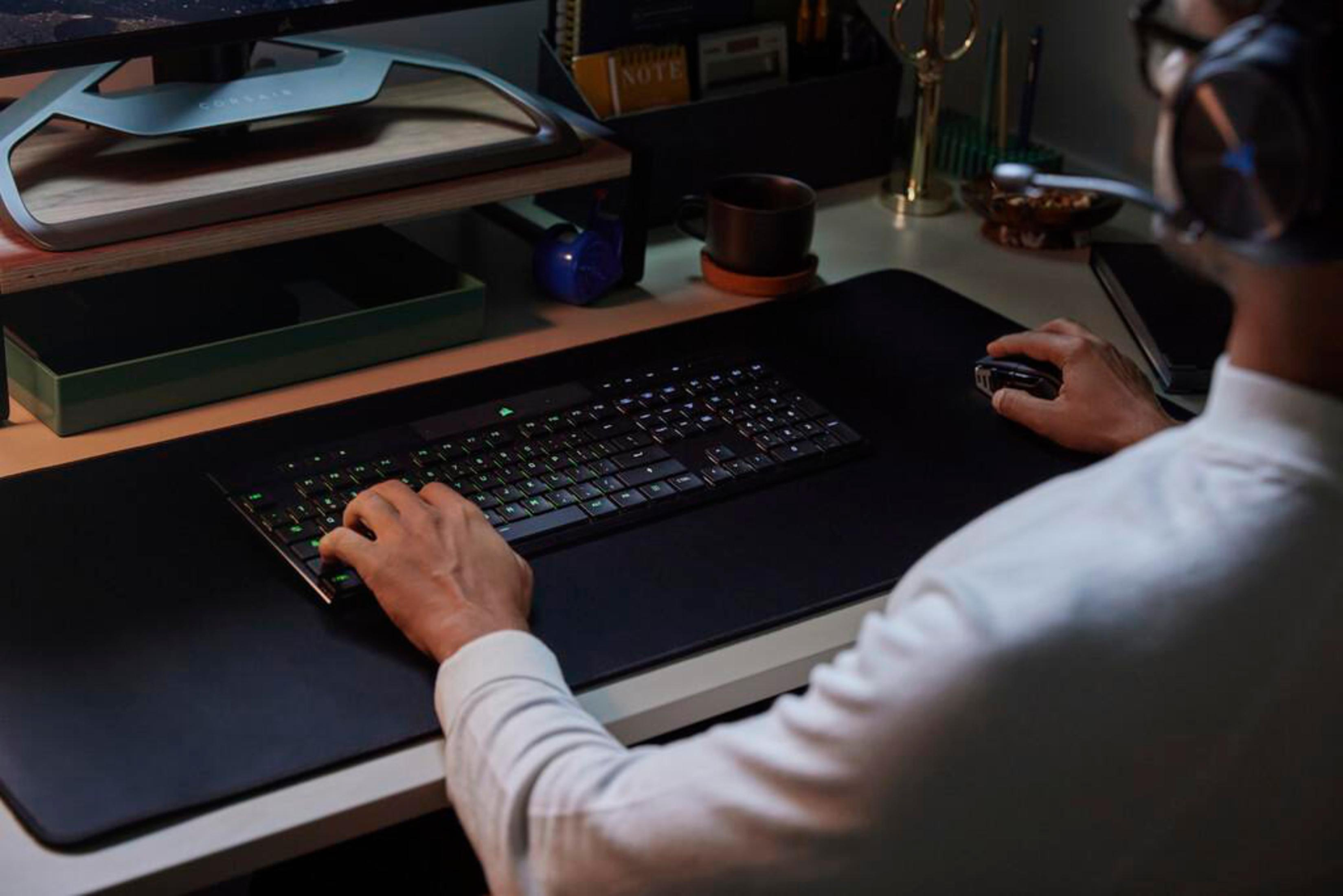 Osoba korzystająca z klawiatury i myszy. Klawiatura ma podświetlane na tęczowo klawisze.