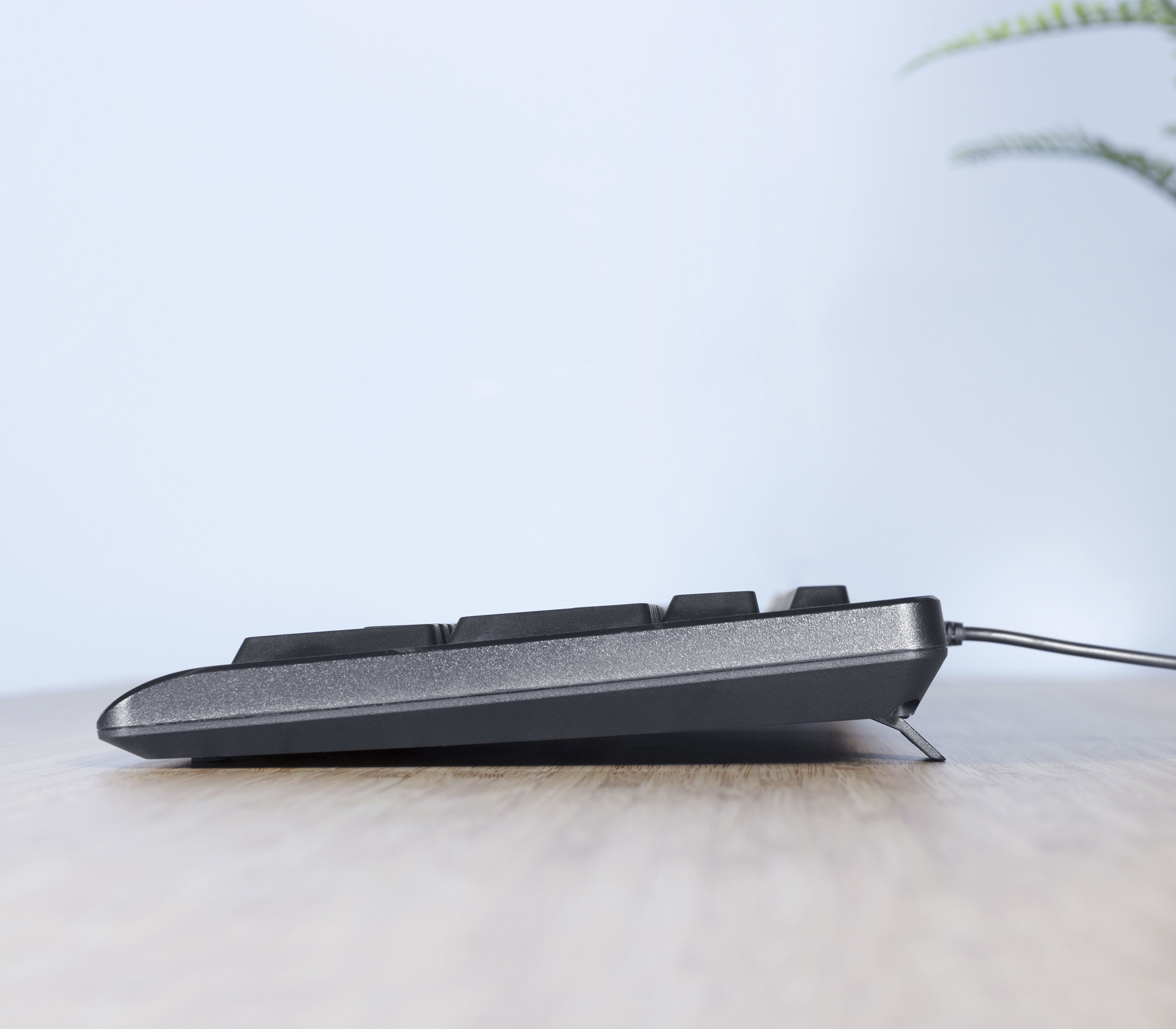Seitenansicht einer schwarzen Tastatur. Die Tastatur steht auf einem Holztisch.