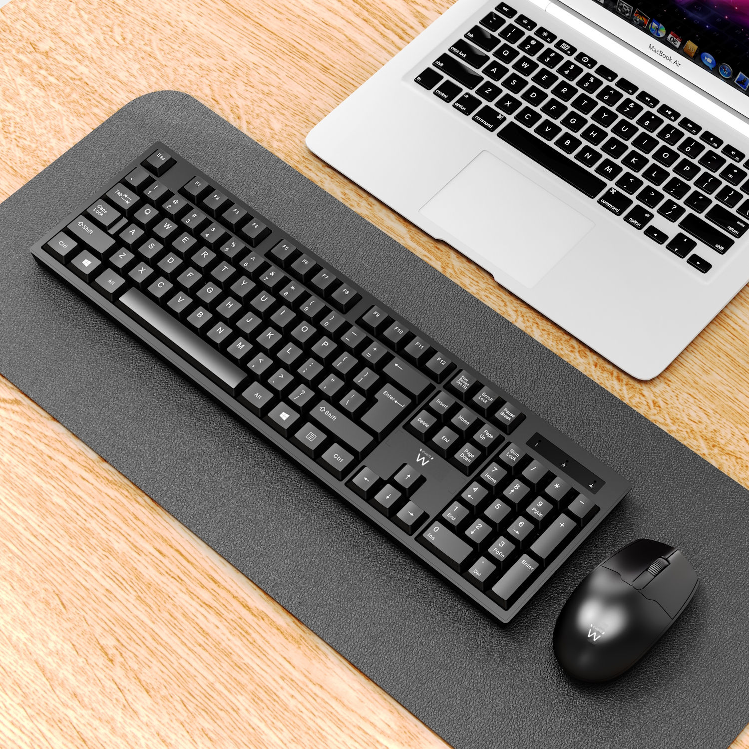Czarna klawiatura i mysz na szarej podkładce z laptopem na drewnianym stole.