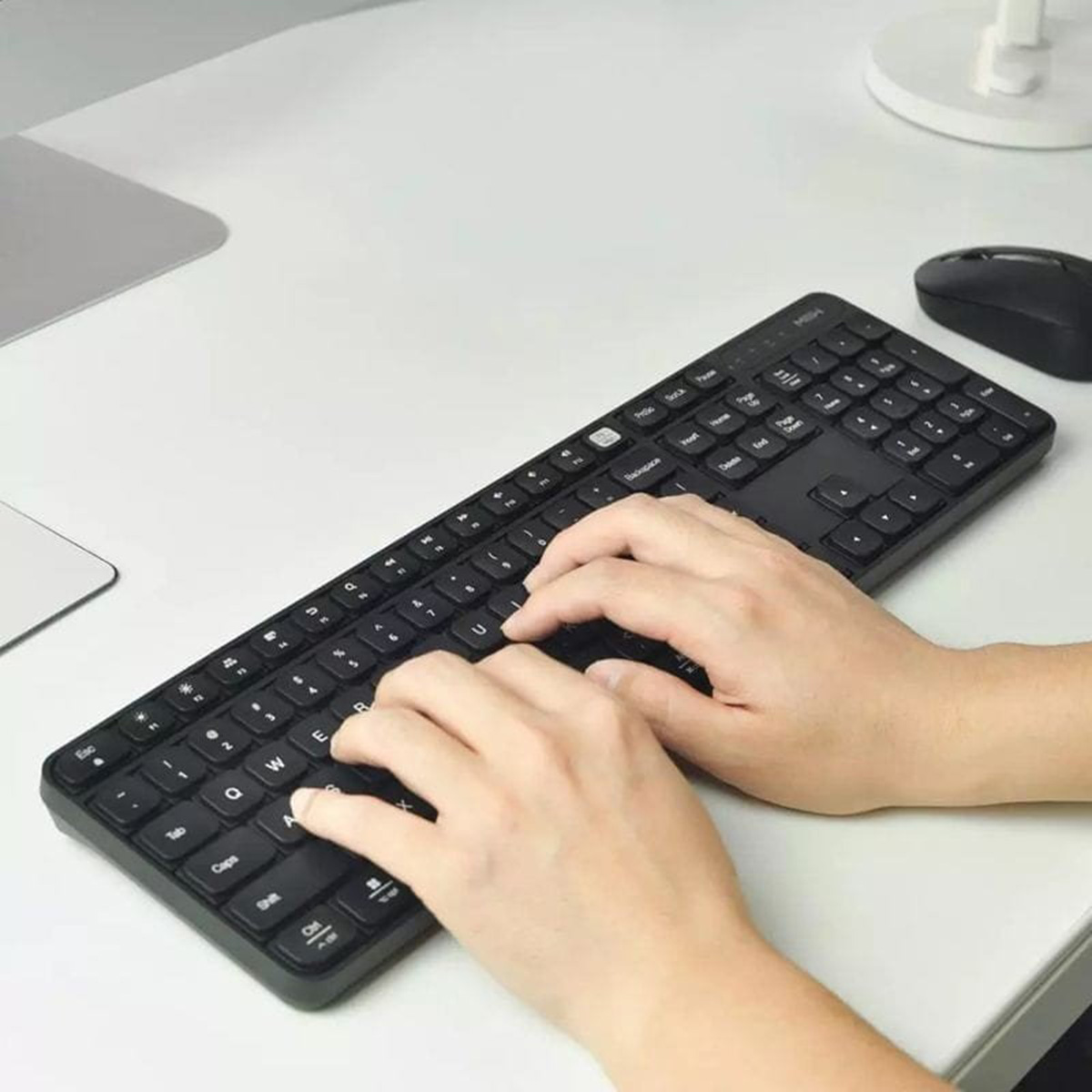Mani che digitano su una tastiera nera su una scrivania bianca con un mouse nero.