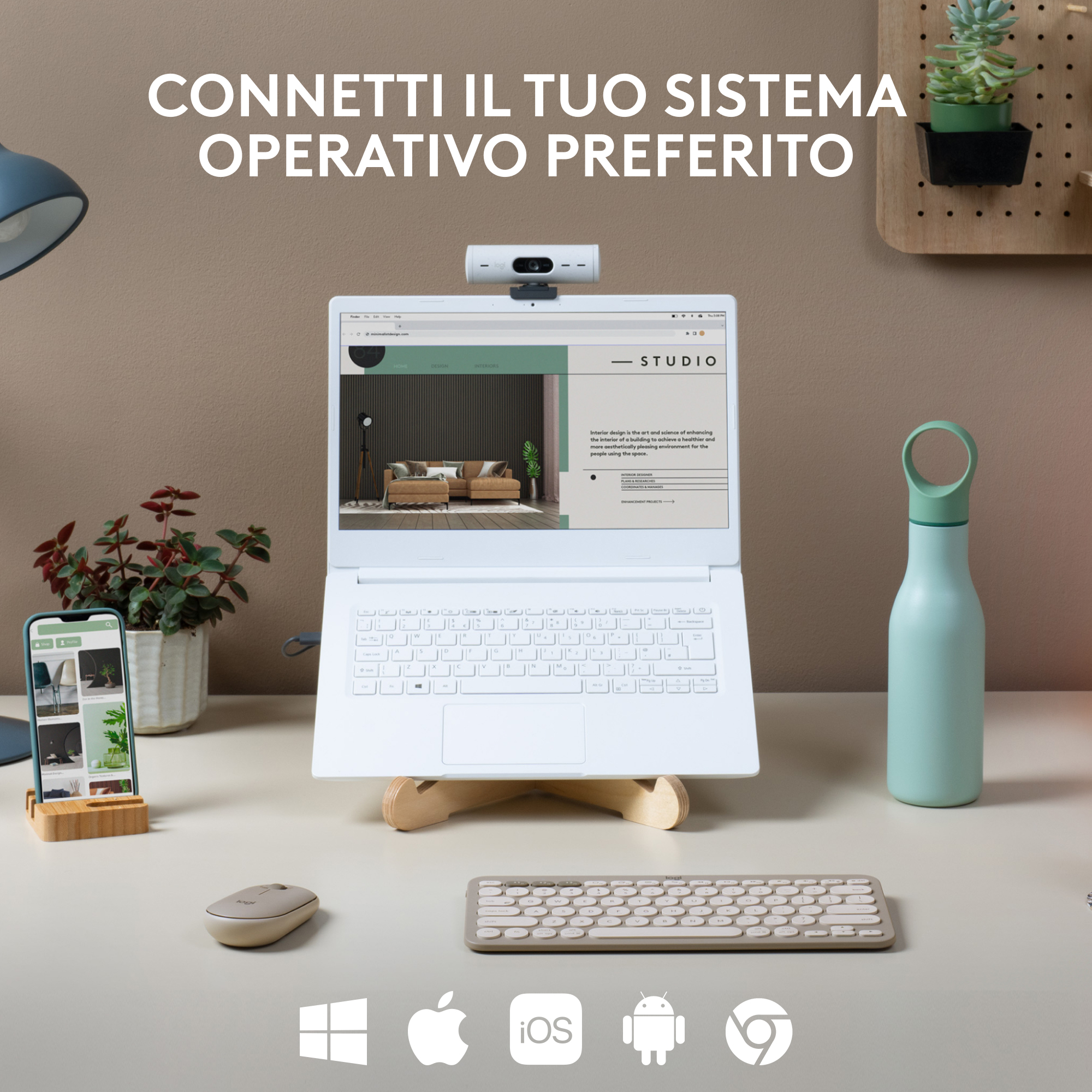 Un laptop su un supporto in legno con una webcam, più un telefono, tastiera e bottiglia.