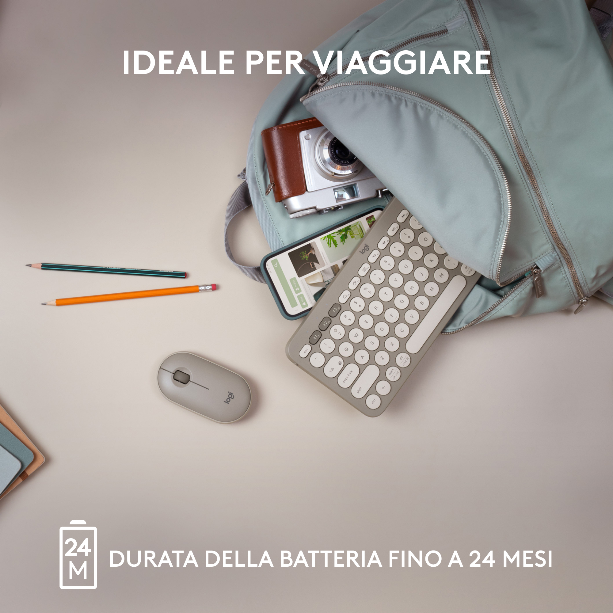 Uno zaino grigio con una fotocamera, telefono, tastiera e mouse all'interno. Ci sono matite accanto.