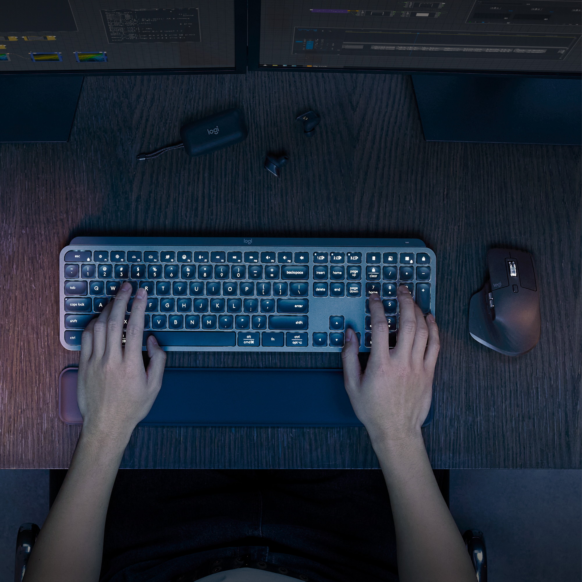 Mani che digitano su una tastiera, con un mouse e monitor sullo sfondo.
