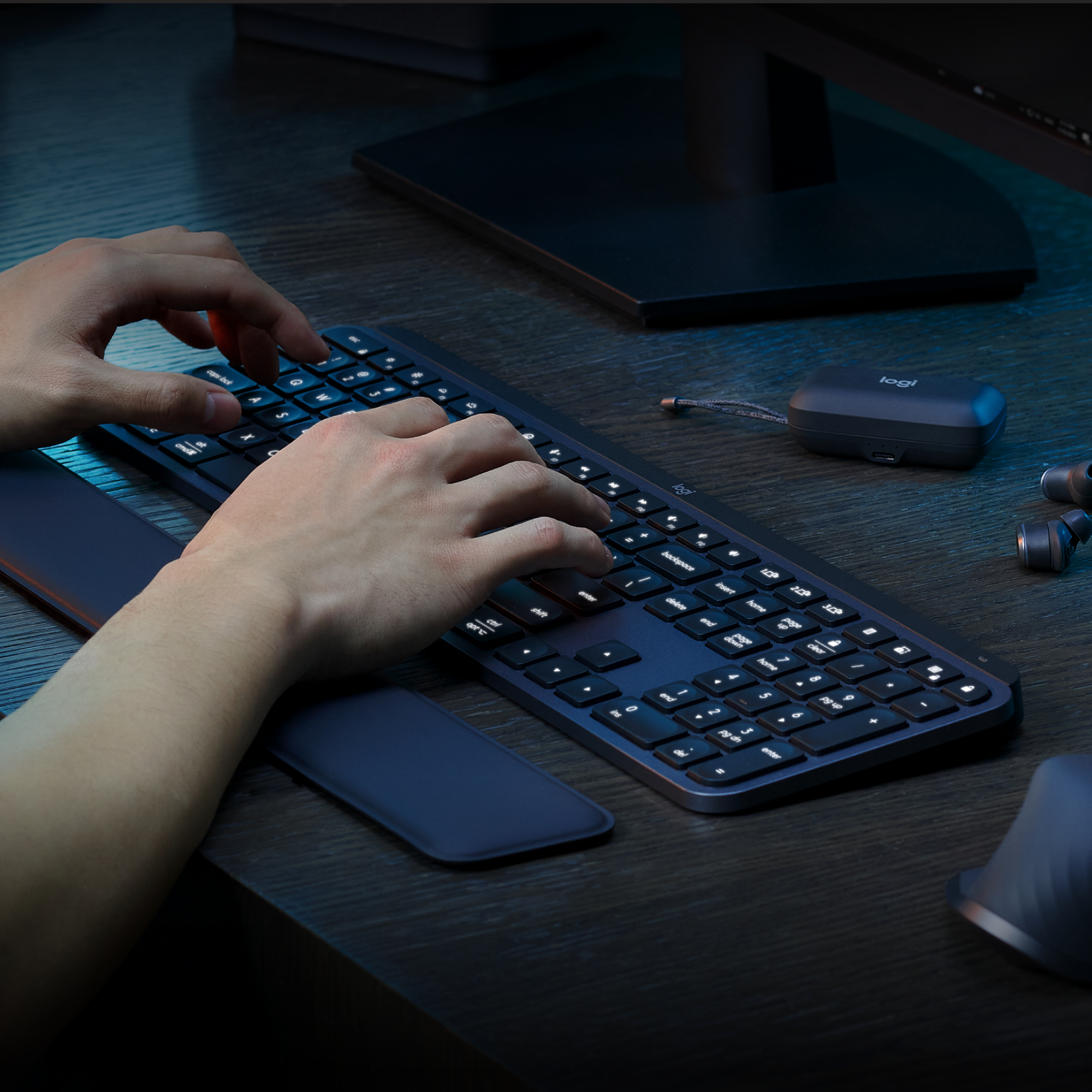 Persona che digita su tastiera nera. Monitor e altri dispositivi sullo sfondo.