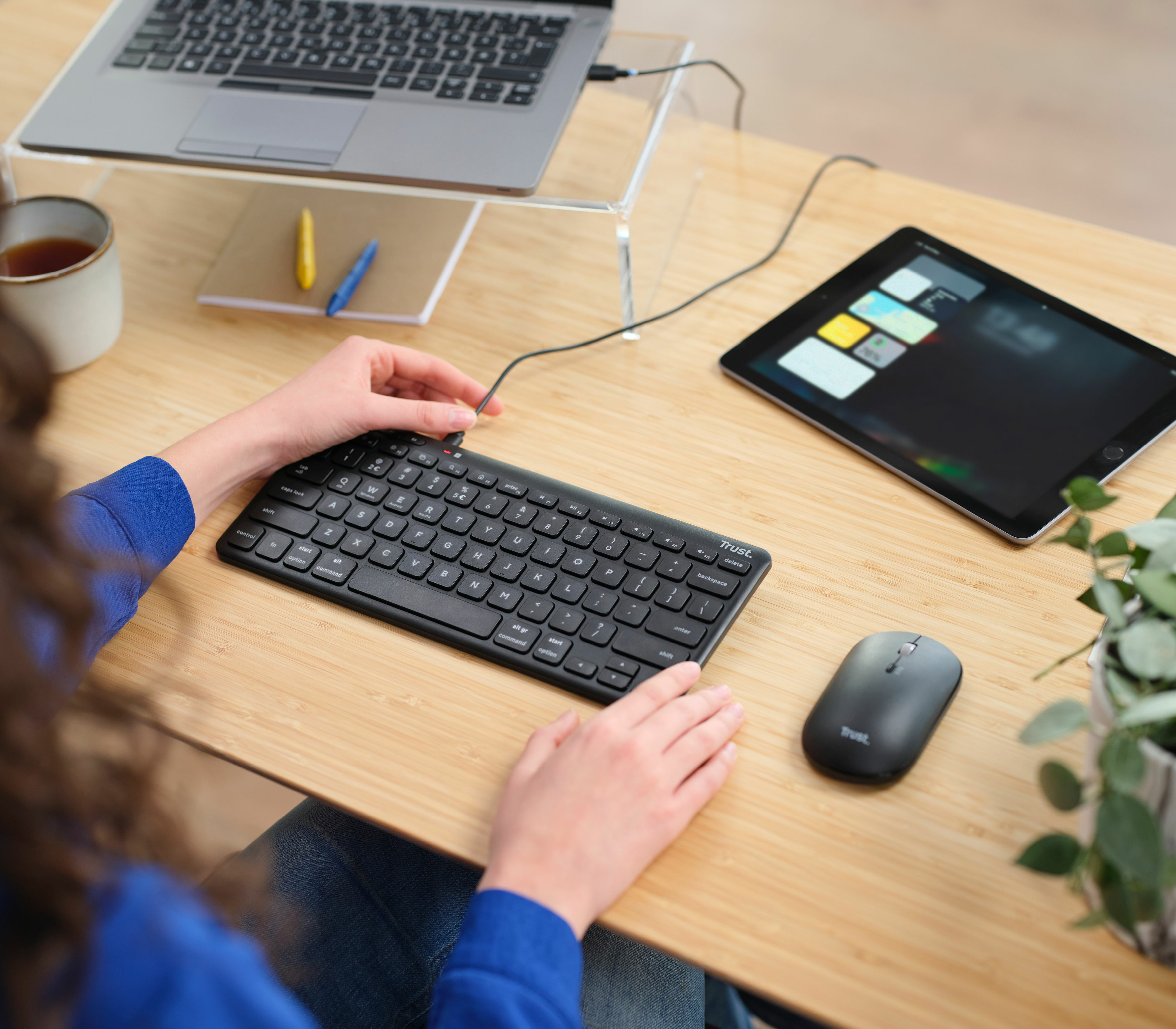Osoba używająca czarnej klawiatury, myszy i tabletu na drewnianym biurku.