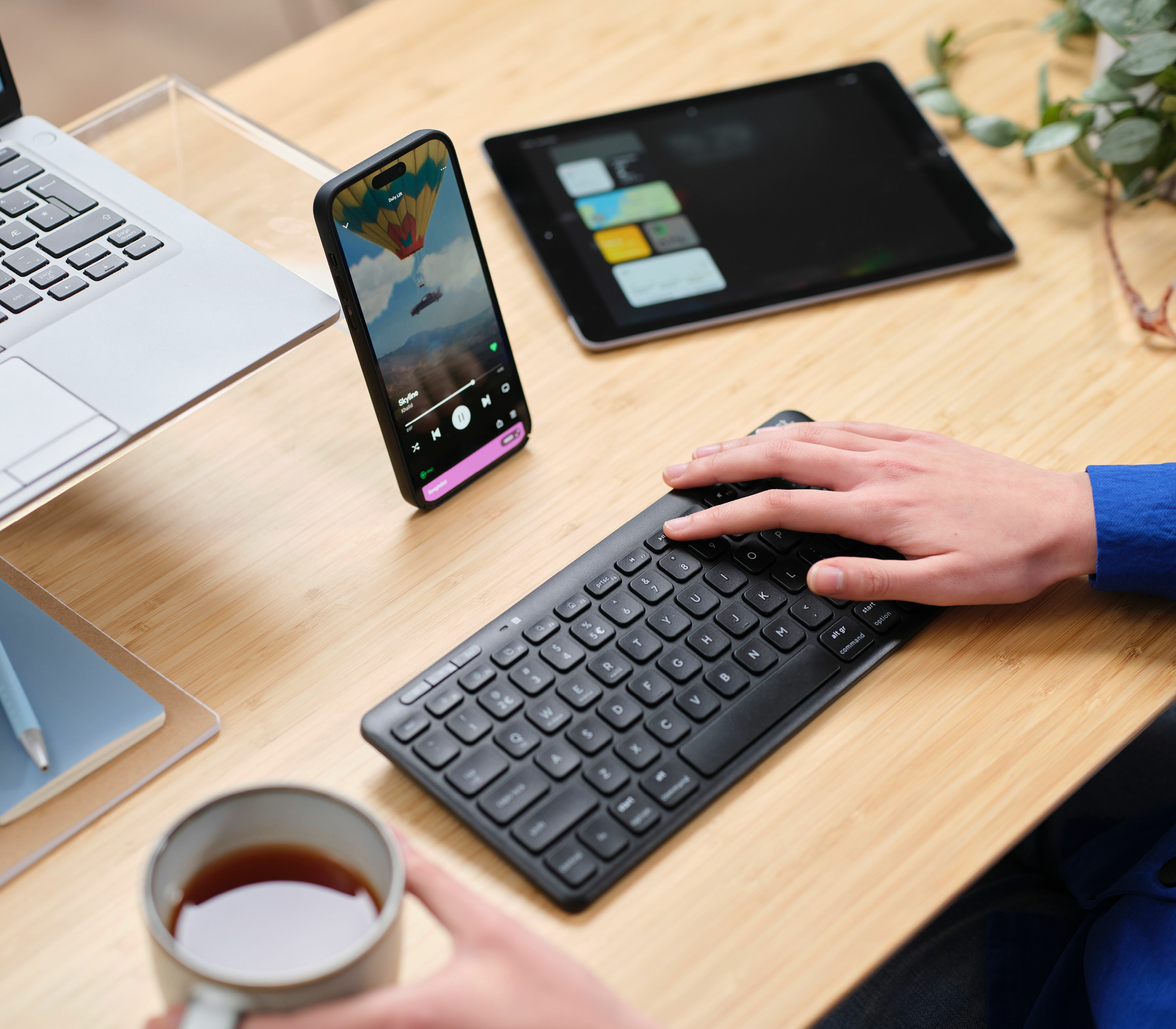 Osoba używająca czarnej klawiatury podłączonej do laptopa i tabletu. Jest filiżanka herbaty.