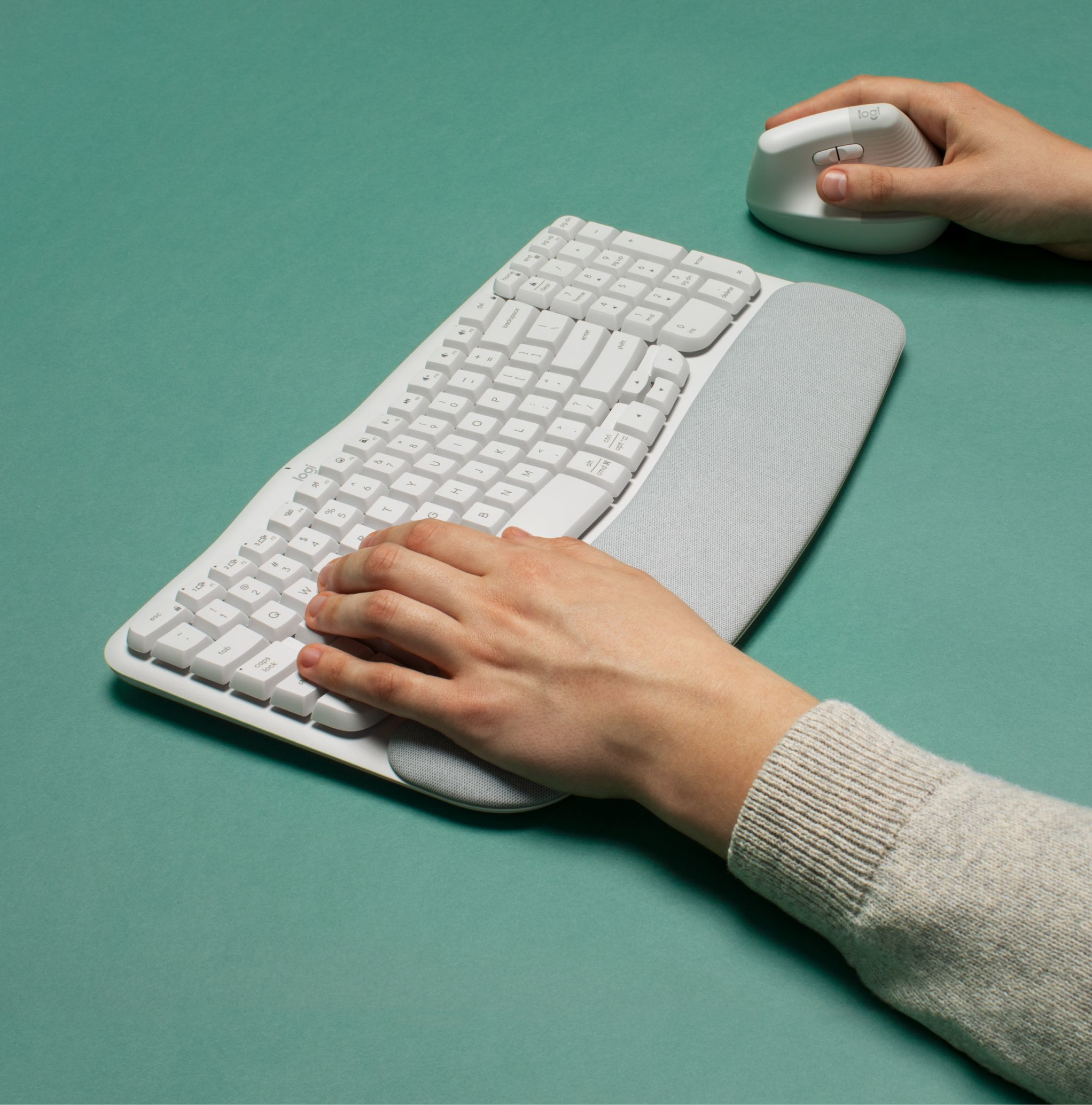 Hände auf einer weißen Tastatur und einer weißen Maus. Die Tastatur hat eine Handballenauflage. Grüner Hintergrund.