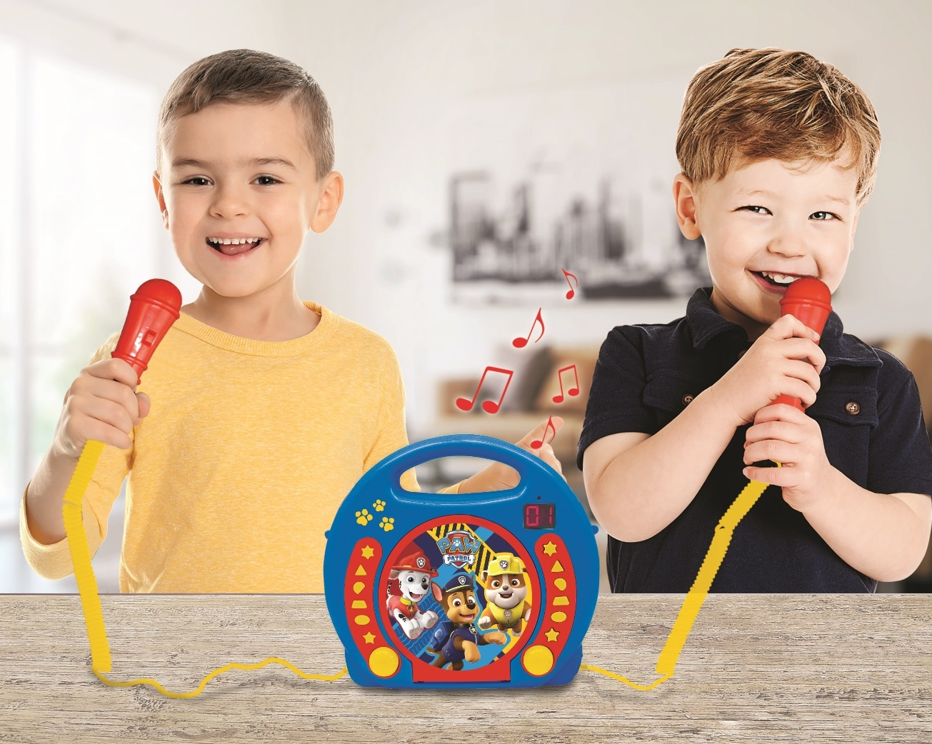 Dwóch uśmiechniętych chłopców z czerwonymi mikrofonami śpiewa. Niebieskie karaoke na stole.