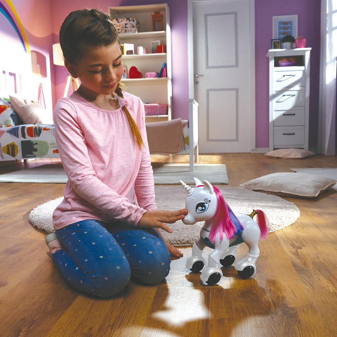 Una bambina in ginocchio tocca un unicorno giocattolo. Il giocattolo ha criniera e coda rosa.