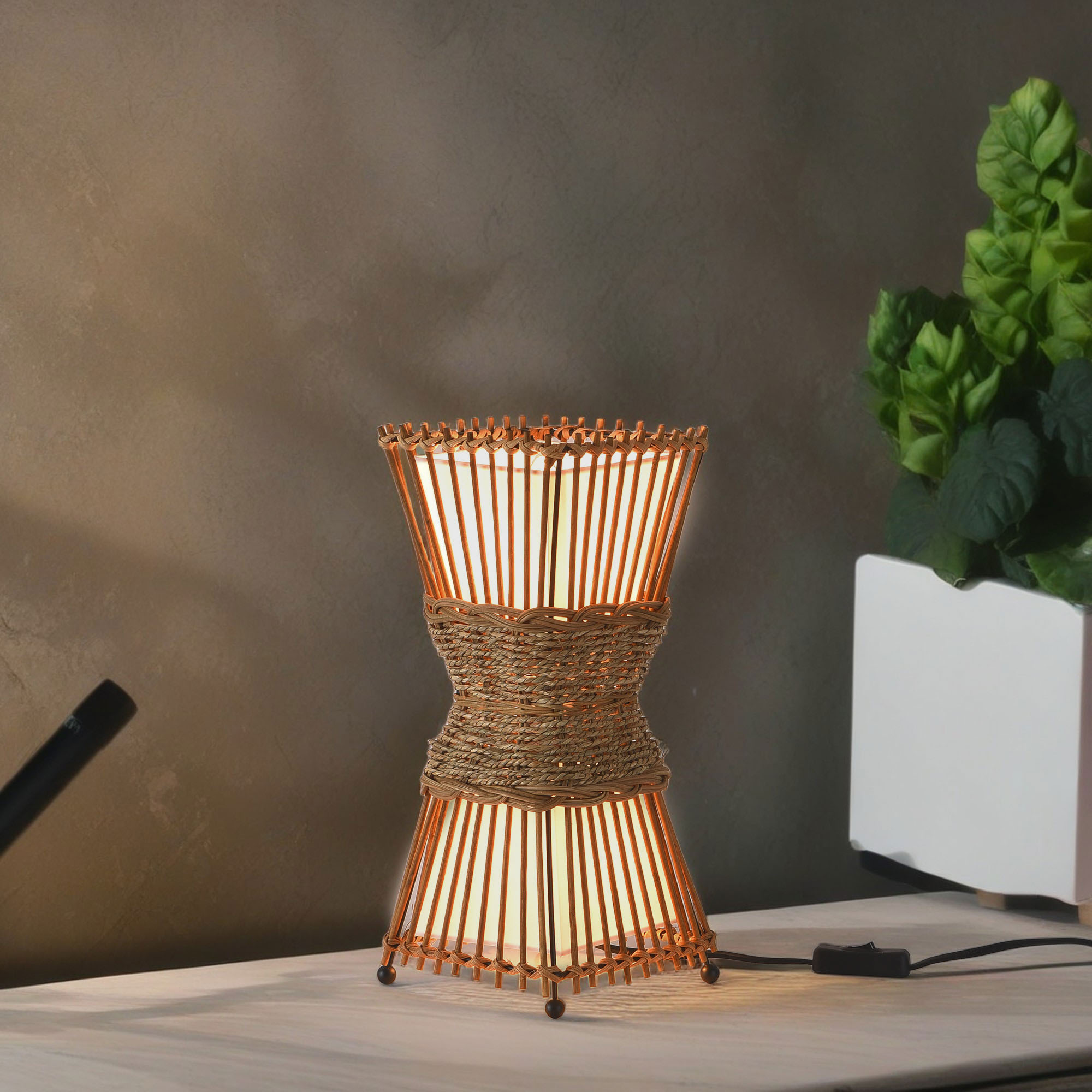 Dekorative Lampe mit gewebter brauner Außenseite und Licht im Inneren. Die Lampe steht auf einem Tisch.