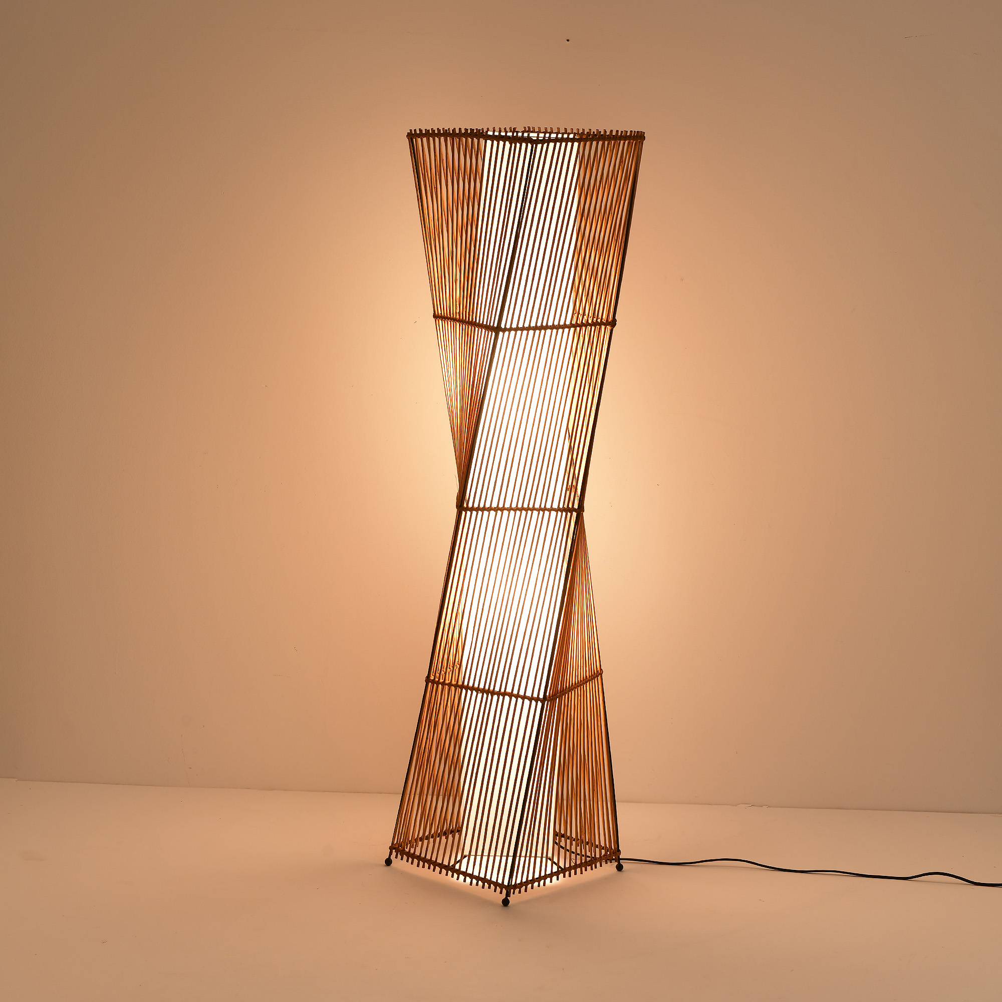 Eine hohe, bambusartige Lampe. Sie wird von innen beleuchtet. Die Form ist eine hohe Drehung.