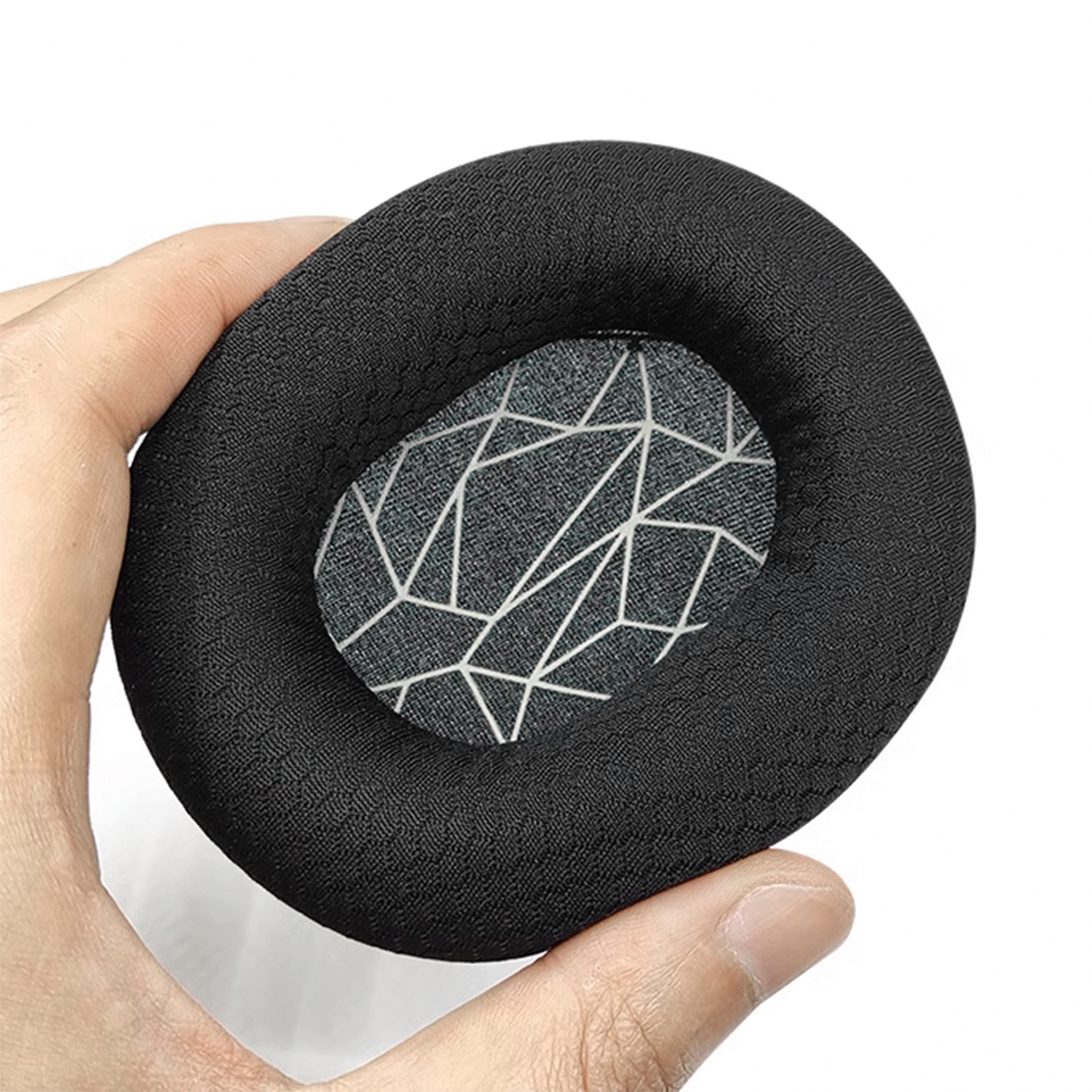 Een zwart schuimrubber oorkussen met een geometrisch stoffen middenstuk, vastgehouden in de hand van een persoon.