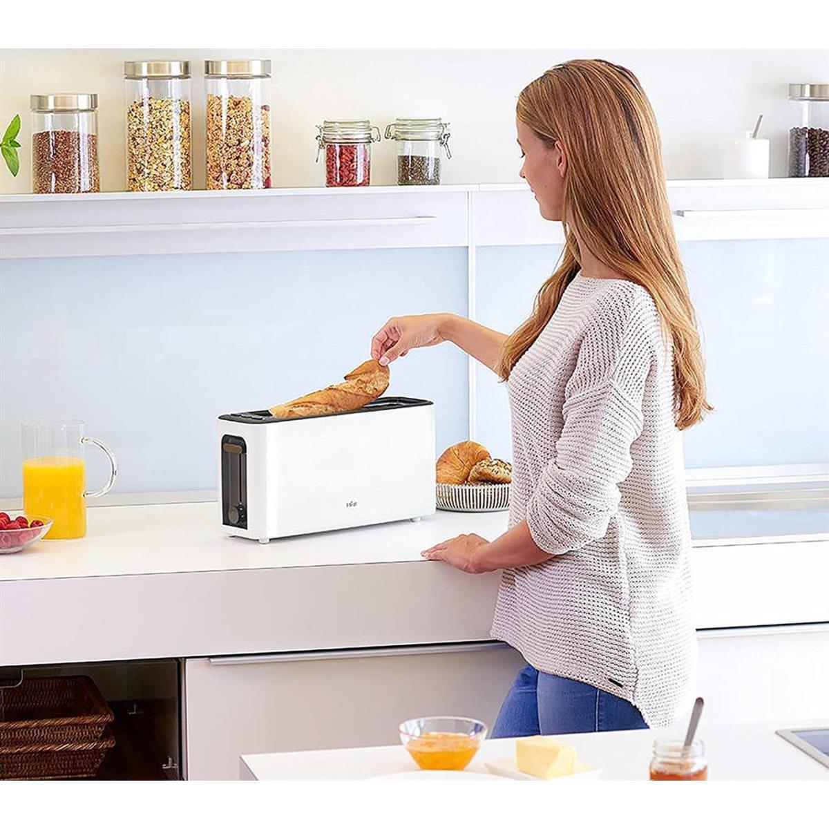 Kobieta z białą tostera, chlebem i słoikami na białym blacie.