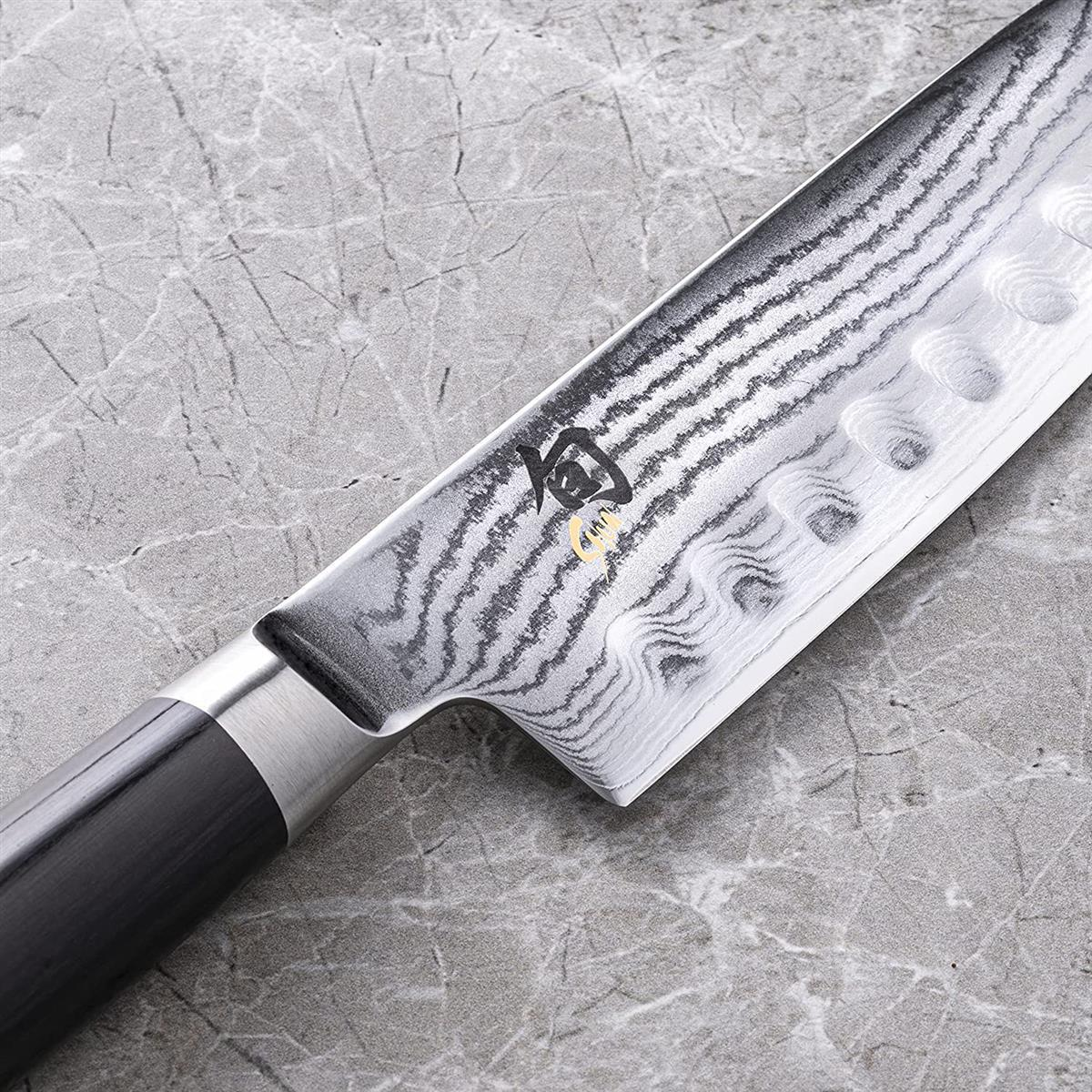 Primo piano di una lama di coltello da cucina con un motivo, su una superficie grigia.