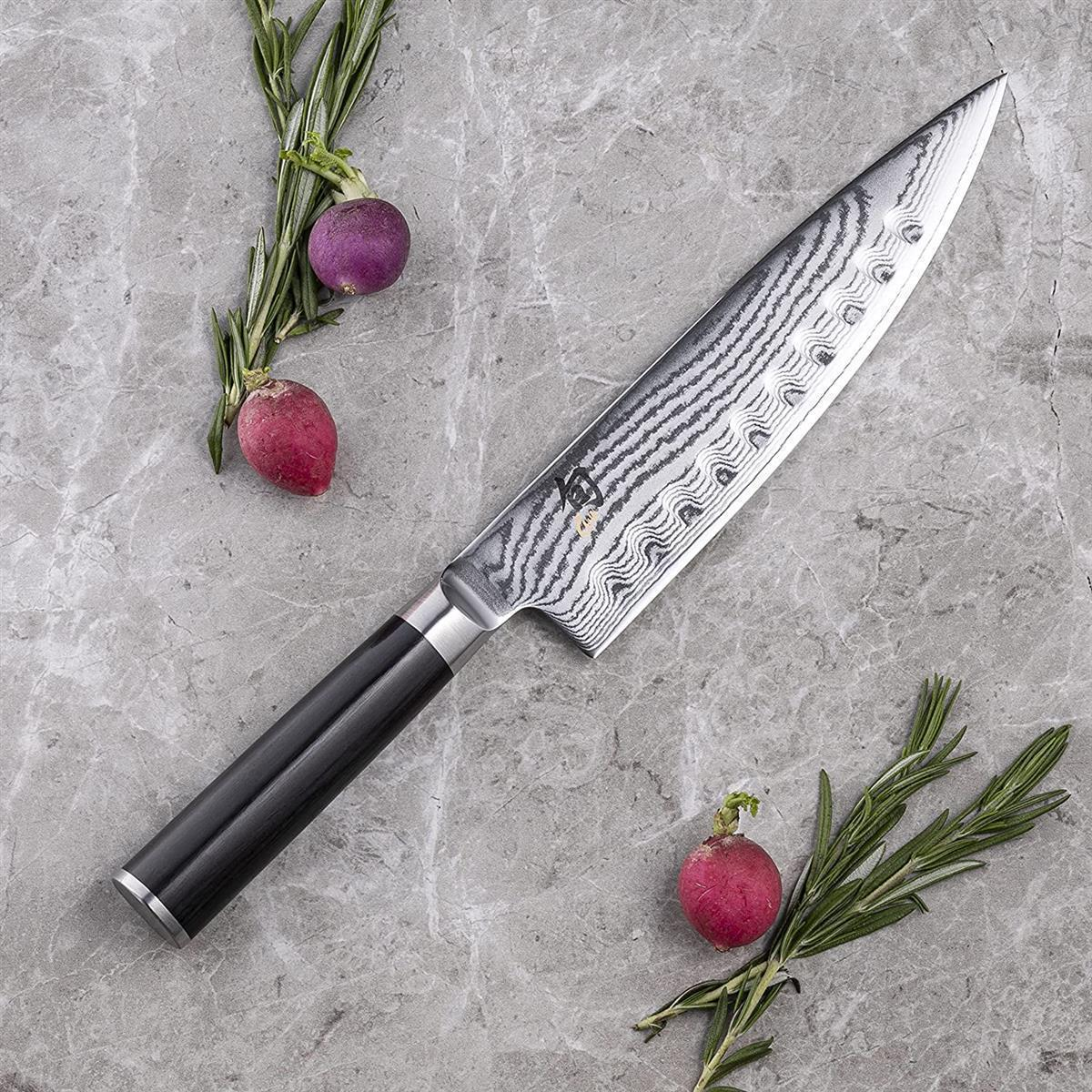 Coltello da chef con motivo di taglio, rosmarino e ravanelli su una superficie di pietra.