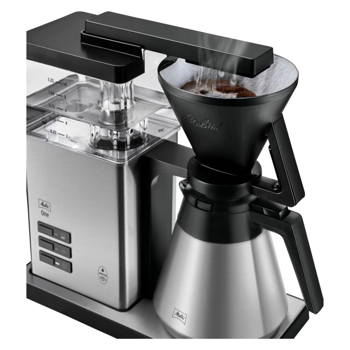 Srebrny ekspres do kawy z czarnym uchwytem na filtr i szklanym dzbankiem. Para jest widoczna.