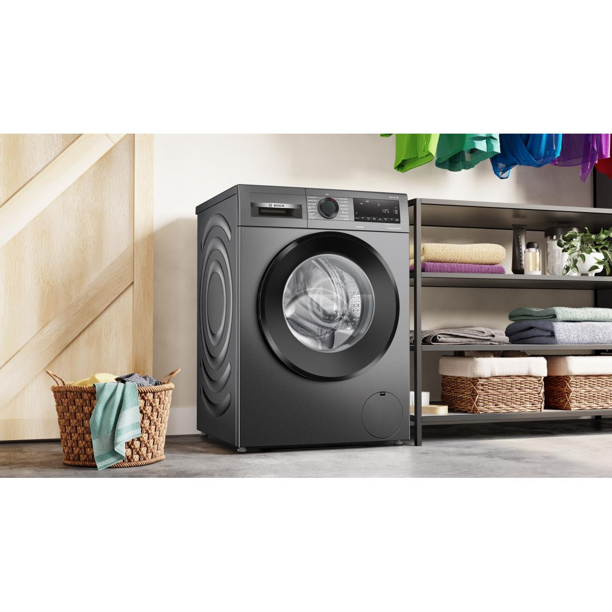 Een donkergrijze wasmachine naast een houten deur. Wasmand en planken met handdoeken in de buurt.
