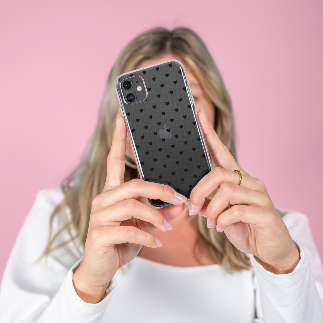 Donna che tiene un telefono con custodia trasparente e piccoli cuori neri su sfondo rosa.
