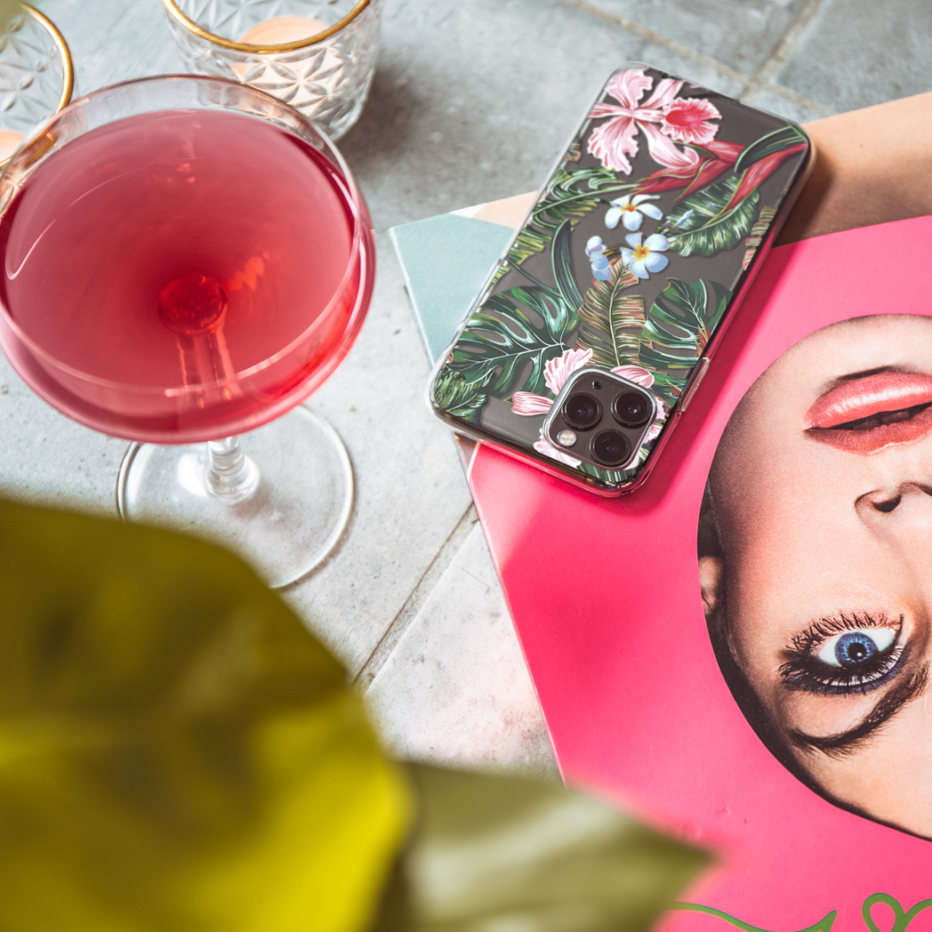 Un cocktail in un bicchiere, una cover per telefono con un design floreale e una rivista.