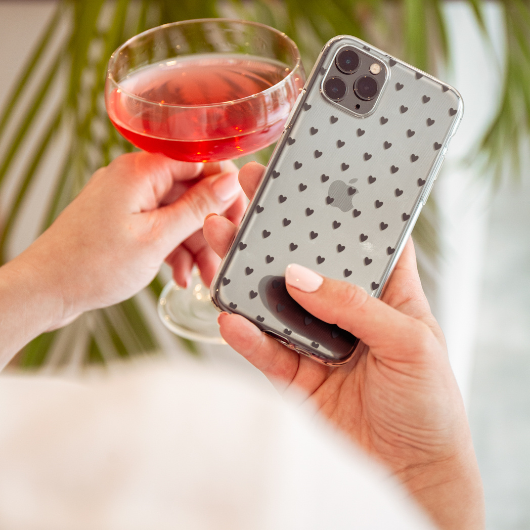 Mani che tengono un telefono con custodia a cuore e un bicchiere da cocktail.