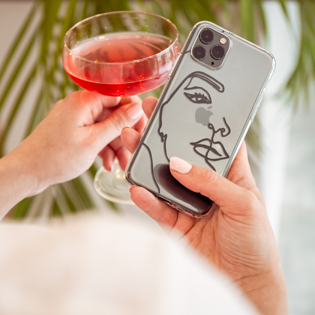 Una persona che tiene una custodia per telefono con un disegno di volto e un bicchiere di vino rosso.