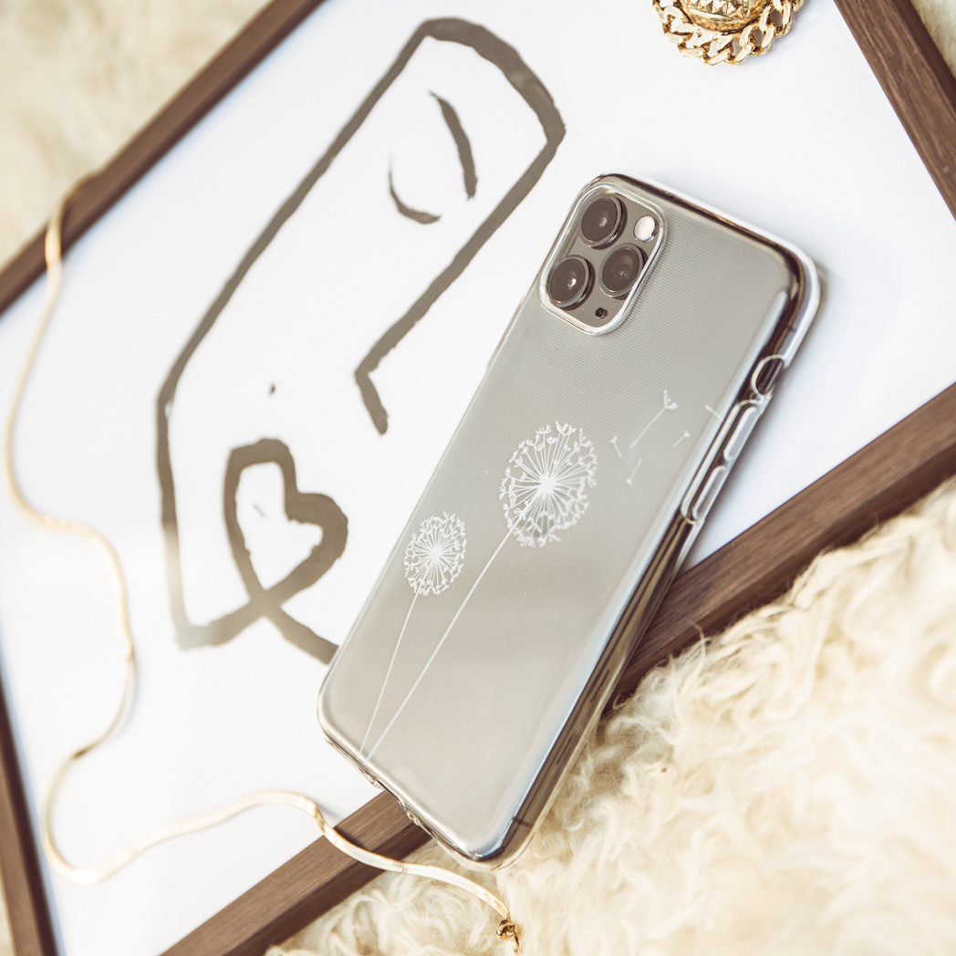 Una custodia per telefono con design di denti di leone, su sfondo bianco, con un quadro e gioielli.
