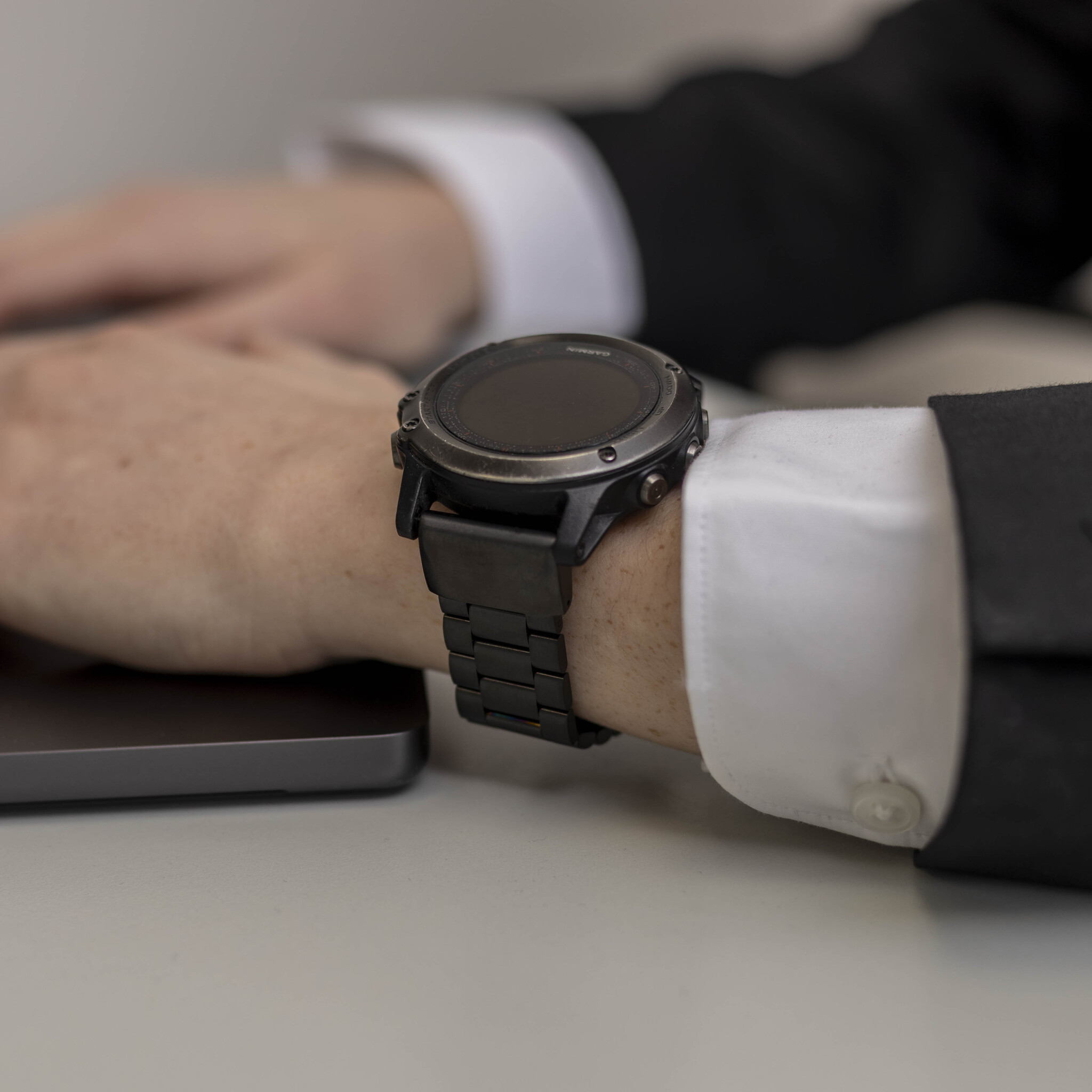Eine Person trägt eine schwarze Uhr am Handgelenk. Die Uhr hat ein schwarzes Metallarmband.